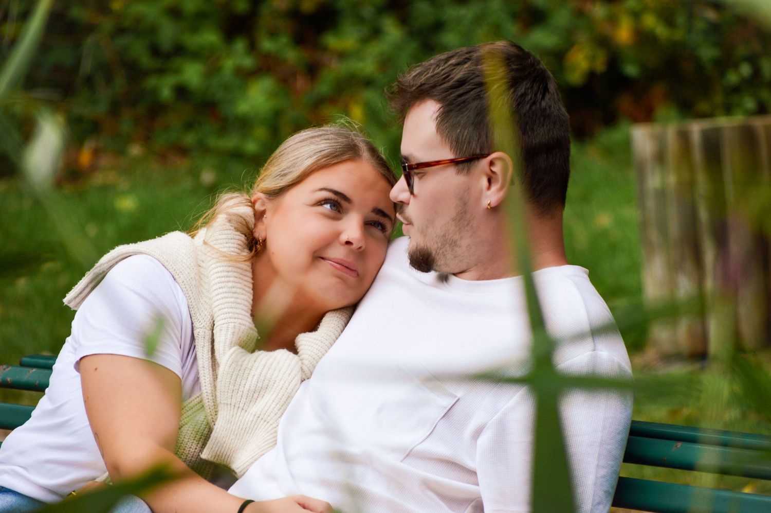 Couple sharing intimate moment on park bench surrounded by greenery.