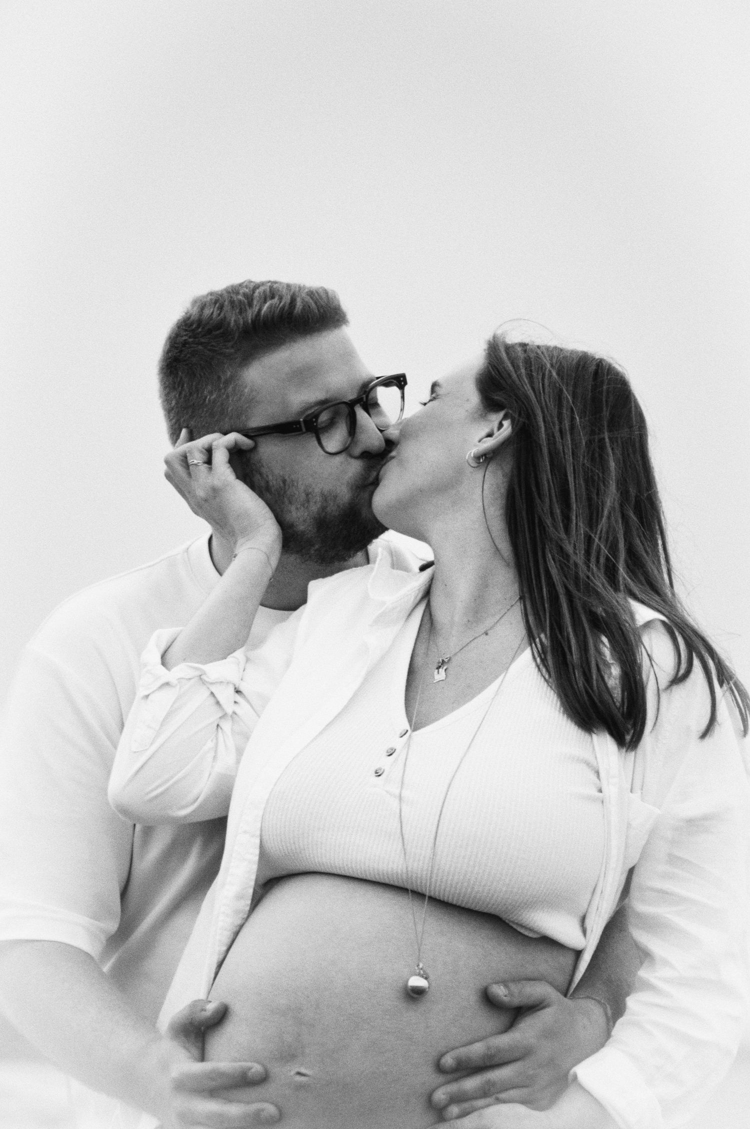 A couple in white shirts shares intimate moments during their maternity photoshoot.