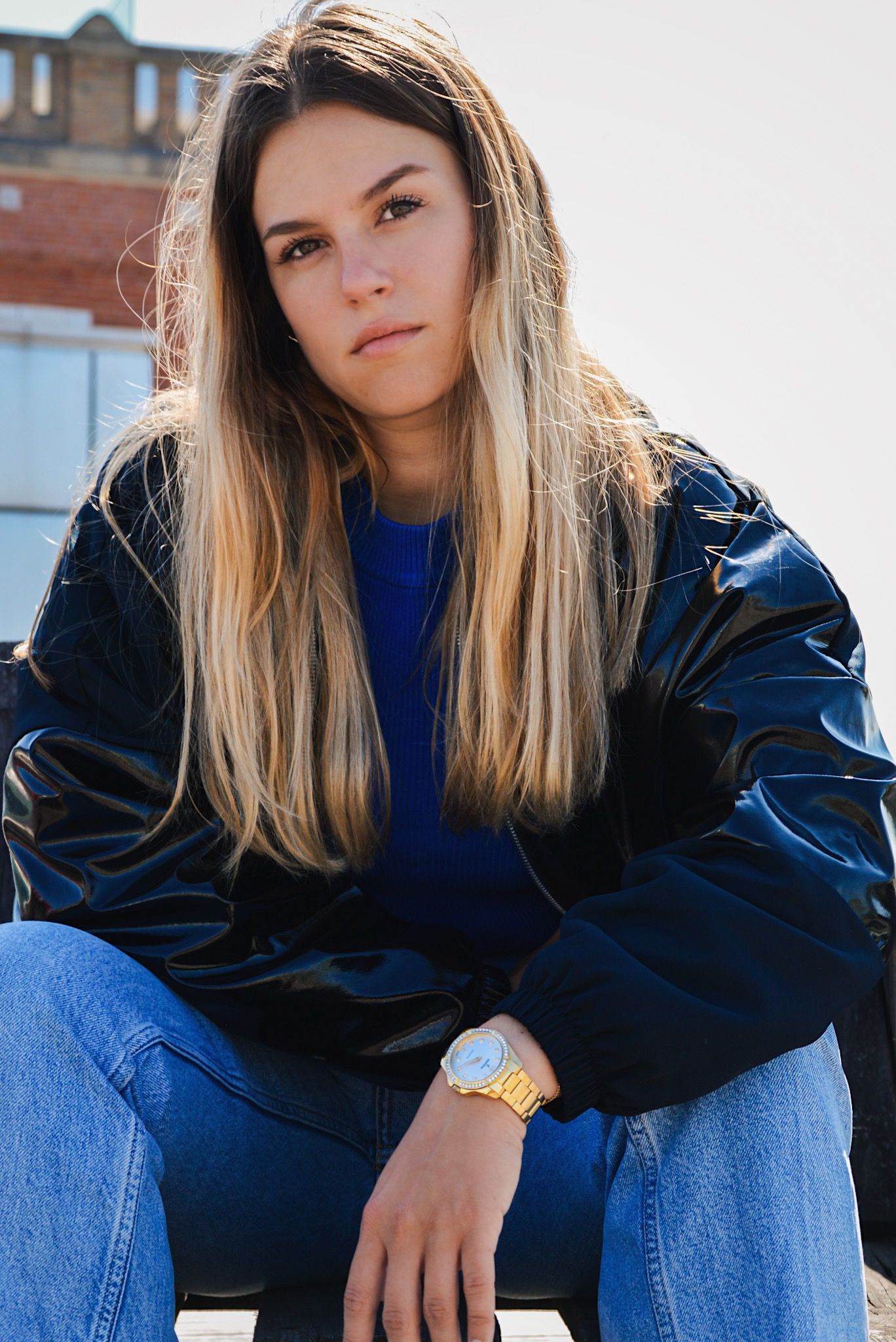 Person in blue top and black jacket sitting casually outdoors.