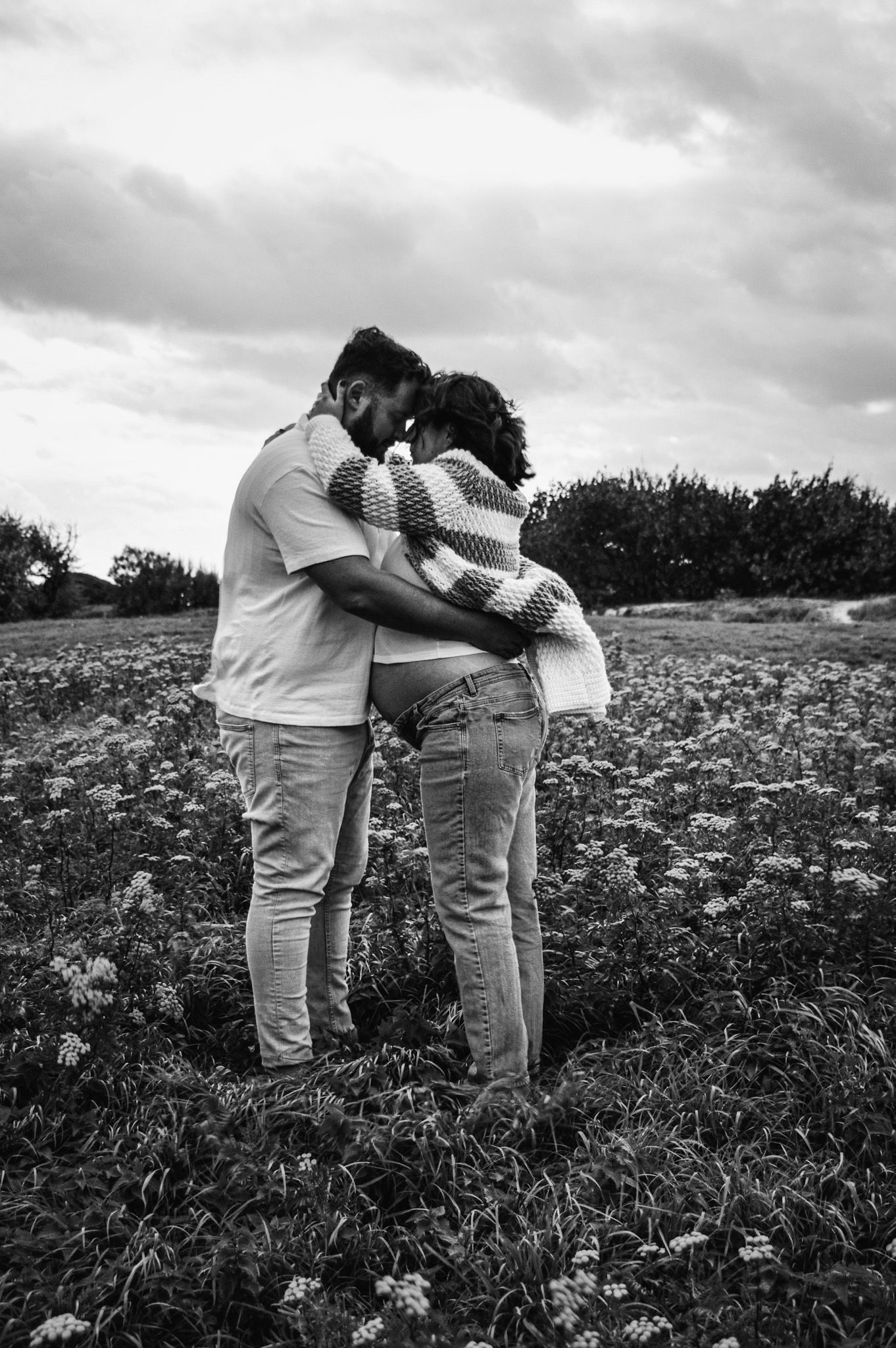Romantic couple embracing in a wildflower field on cloudy day.