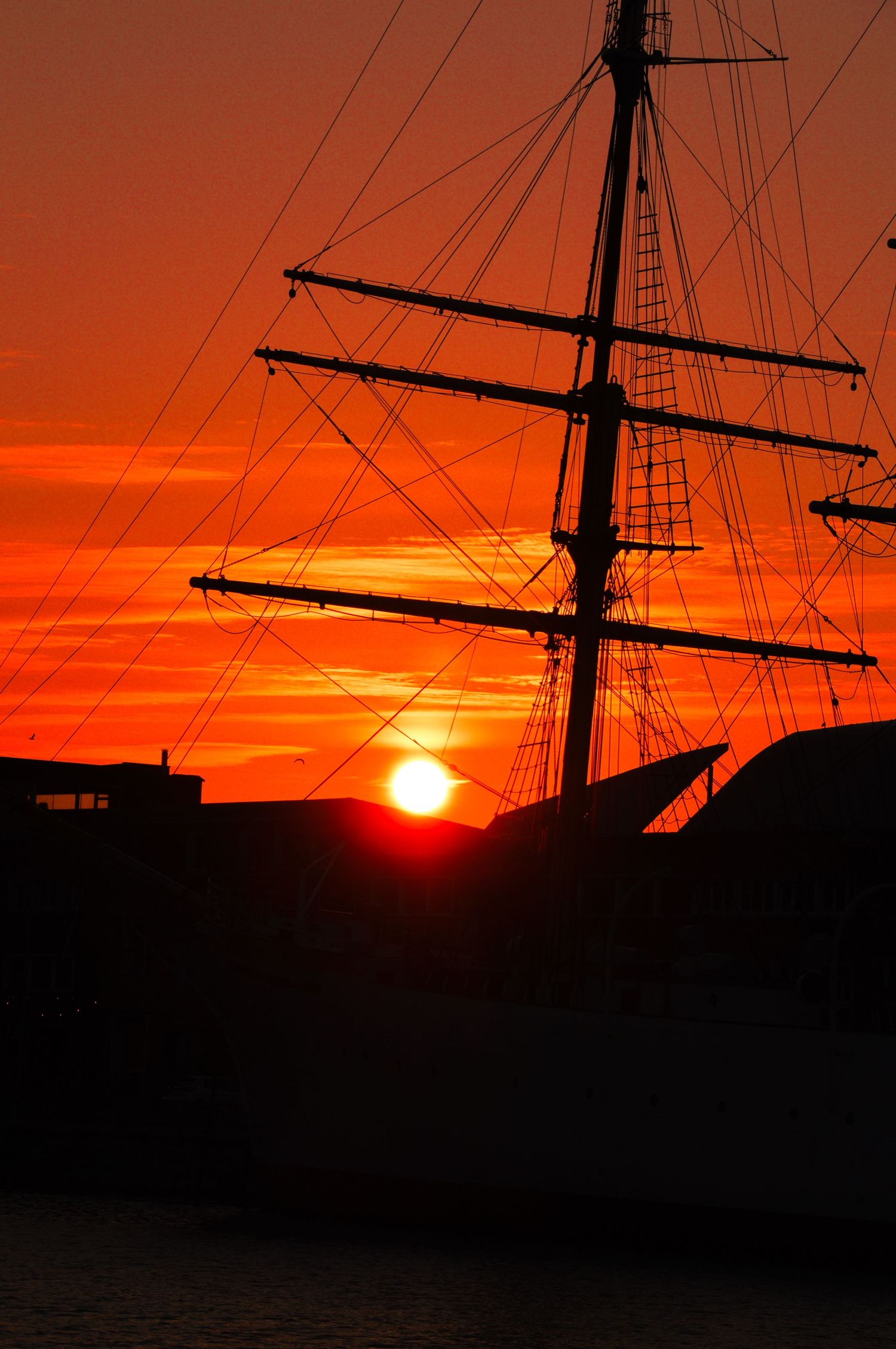 Mâts et gréements du voilier de la Duchesse-anne formant une silhouette spectaculaire sur un ciel de coucher de soleil orange flamboyant.