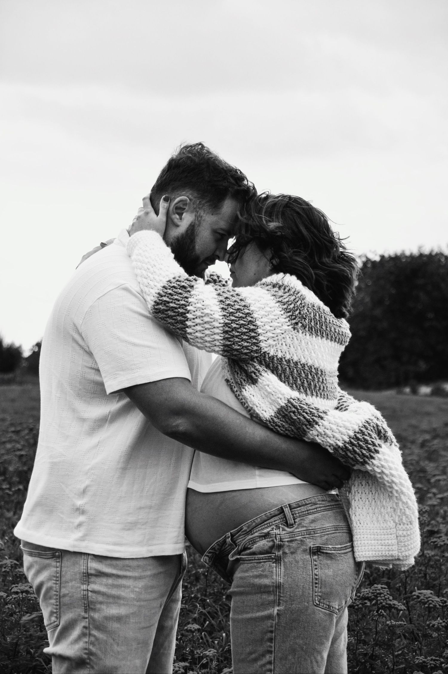 Two people share an intimate moment wrapped in a knit blanket outdoors.