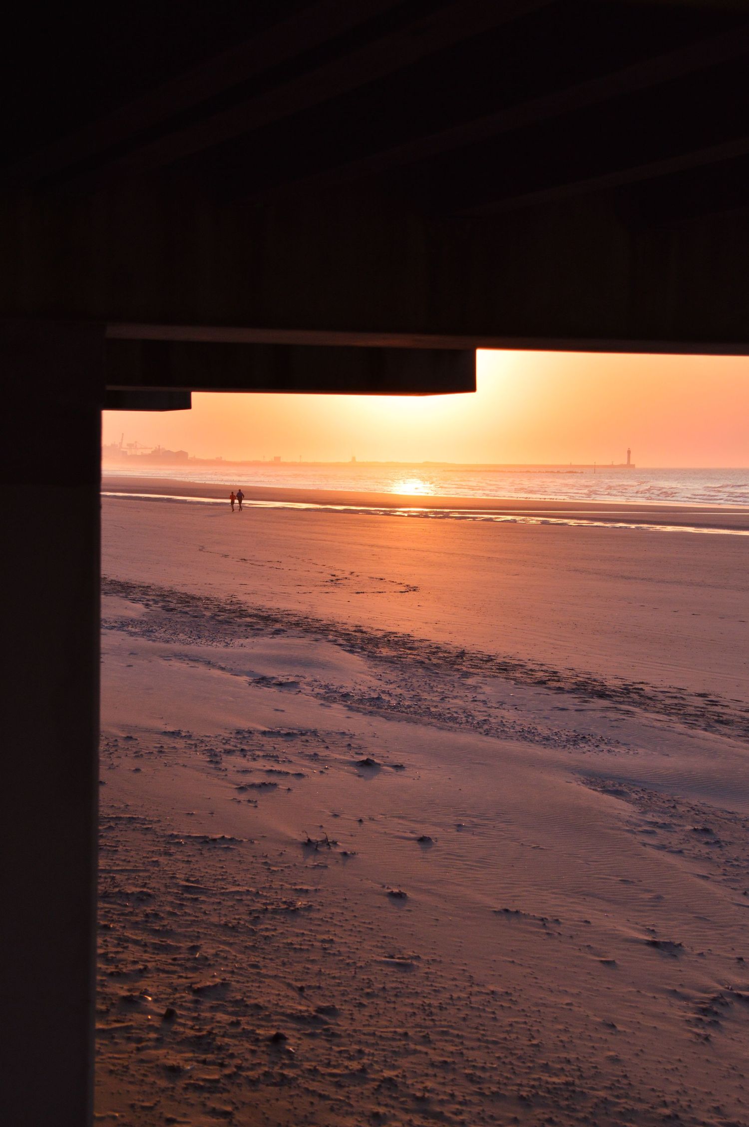 Sunset view of a beach through an underpass frame with silhouettes in the distance.