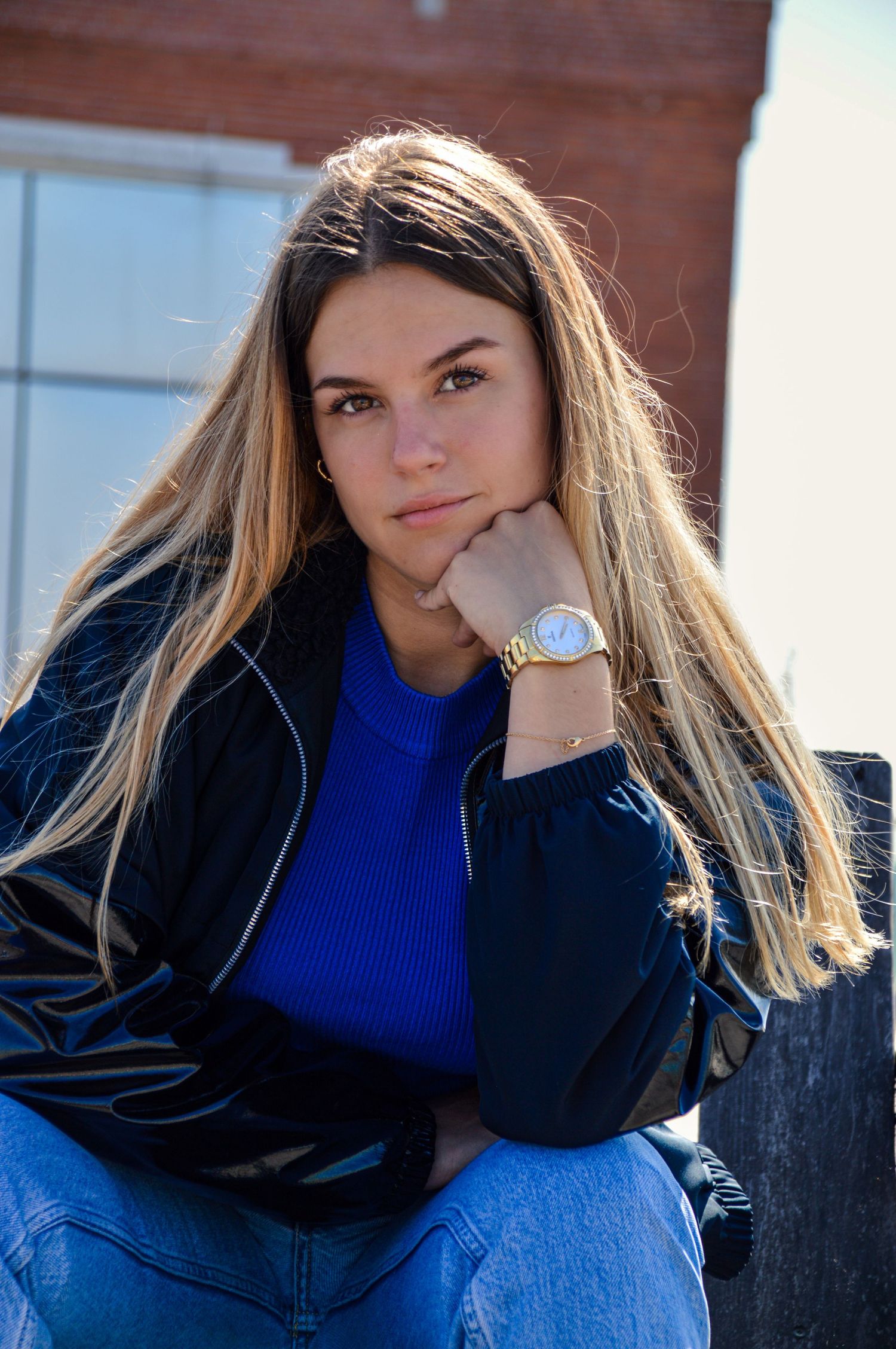 Portrait series of person in blue sweater and black jacket against brick wall.