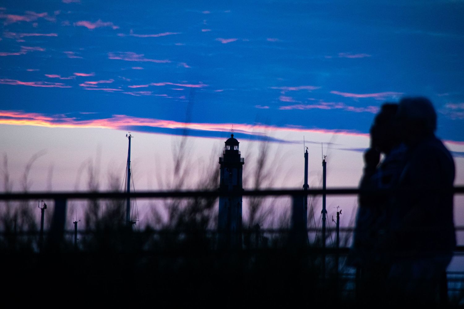 Silhouette of person and lighthouse against vibrant blue and pink sunset sky at dusk.