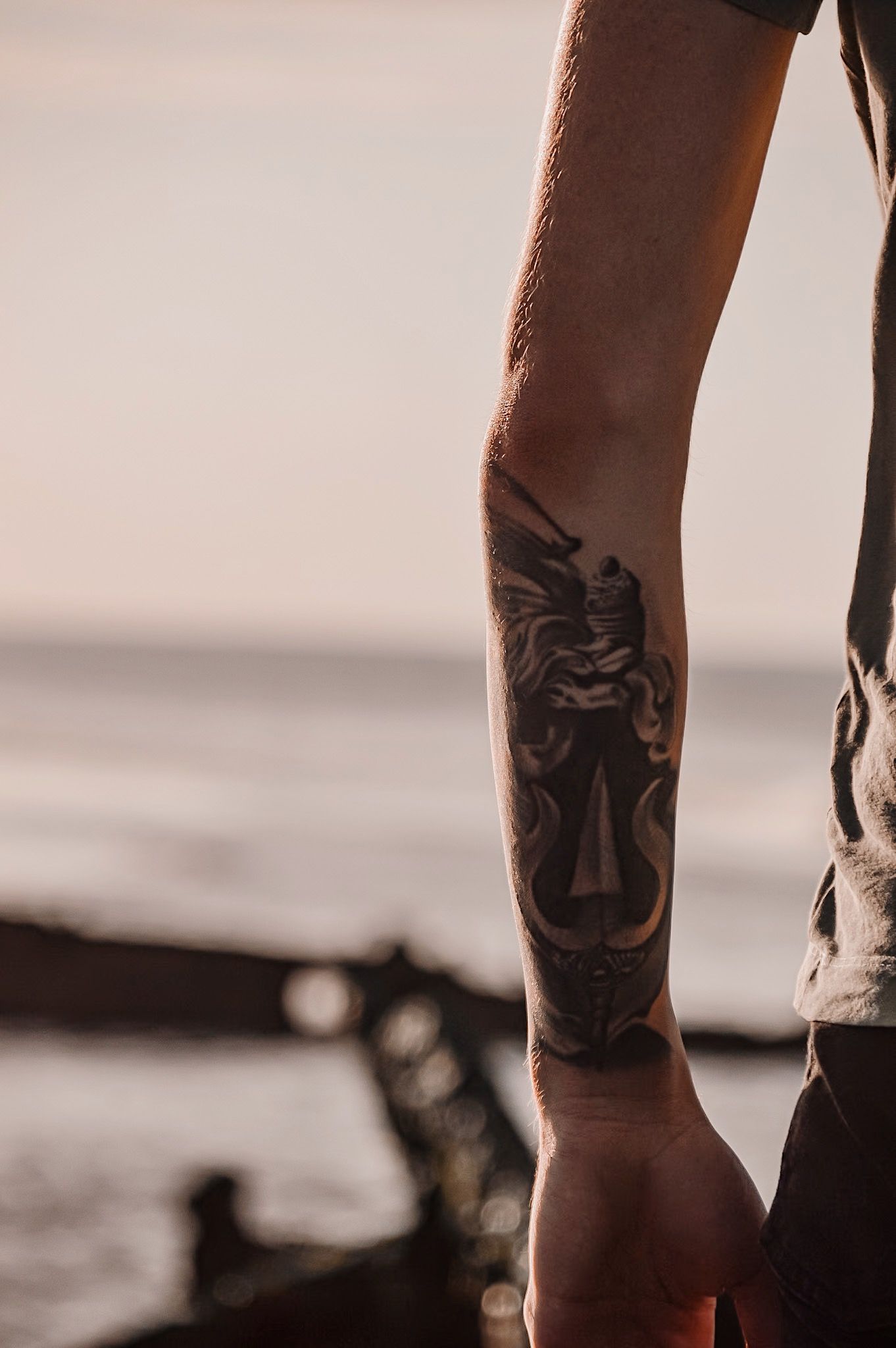 Close-up of arm tattoo silhouetted against sunset ocean view.
