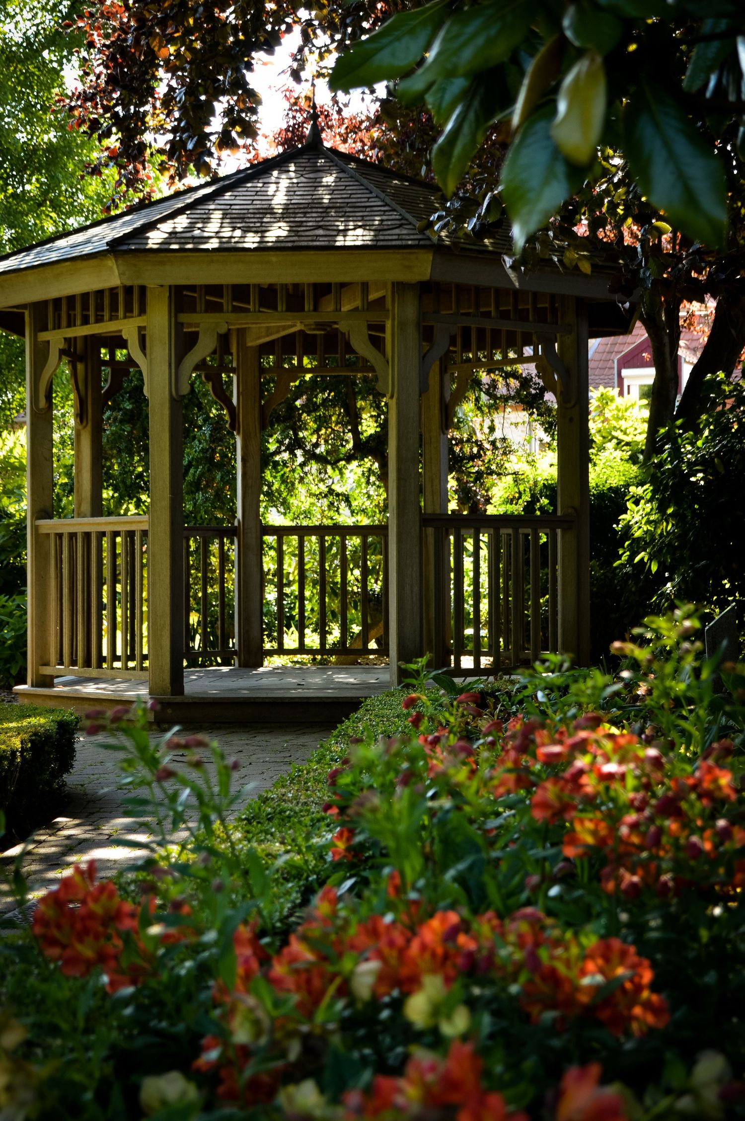 A series of wooden gazebos nestled among colorful flowers and green foliage in a garden setting.