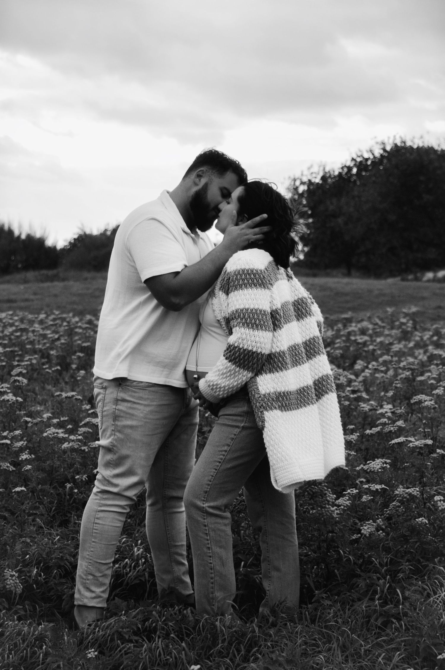 Black and white maternity photos in blooming wildflower field.