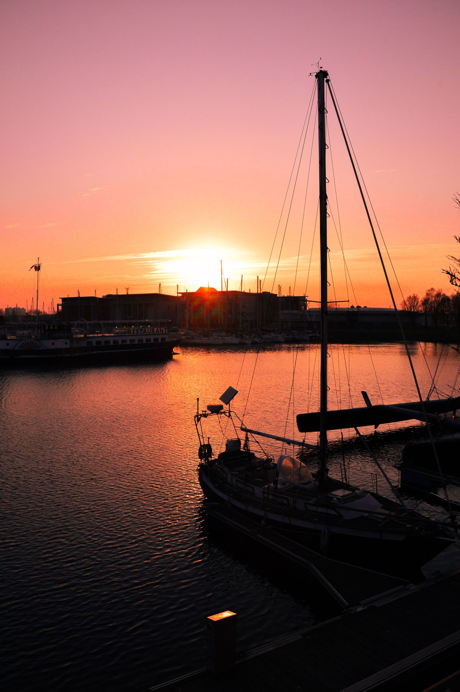 Silhouettes of docked boats against pink and orange sunset sky over marina.
