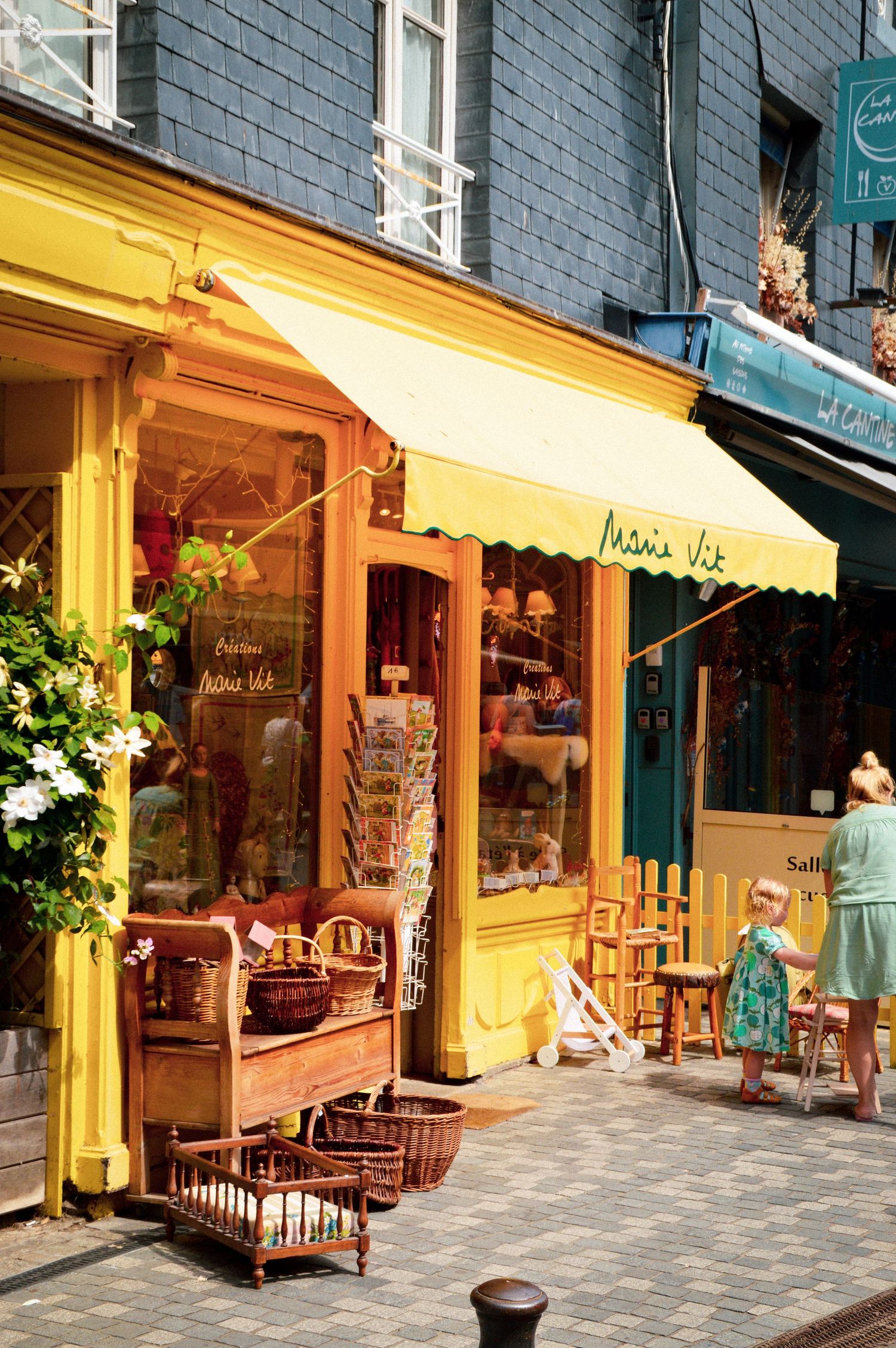 Row of colorful storefronts with yellow awnings and outdoor displays on a shopping street.