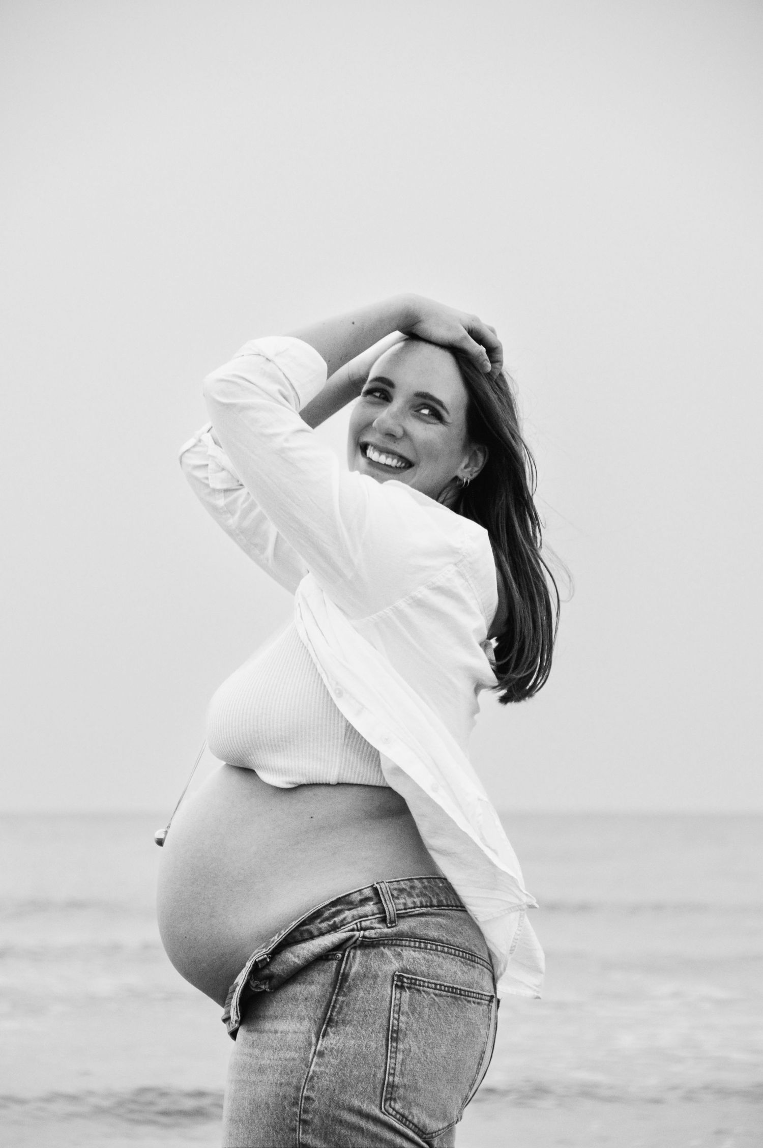Artistic black and white maternity photos showing joyful poses by the ocean.