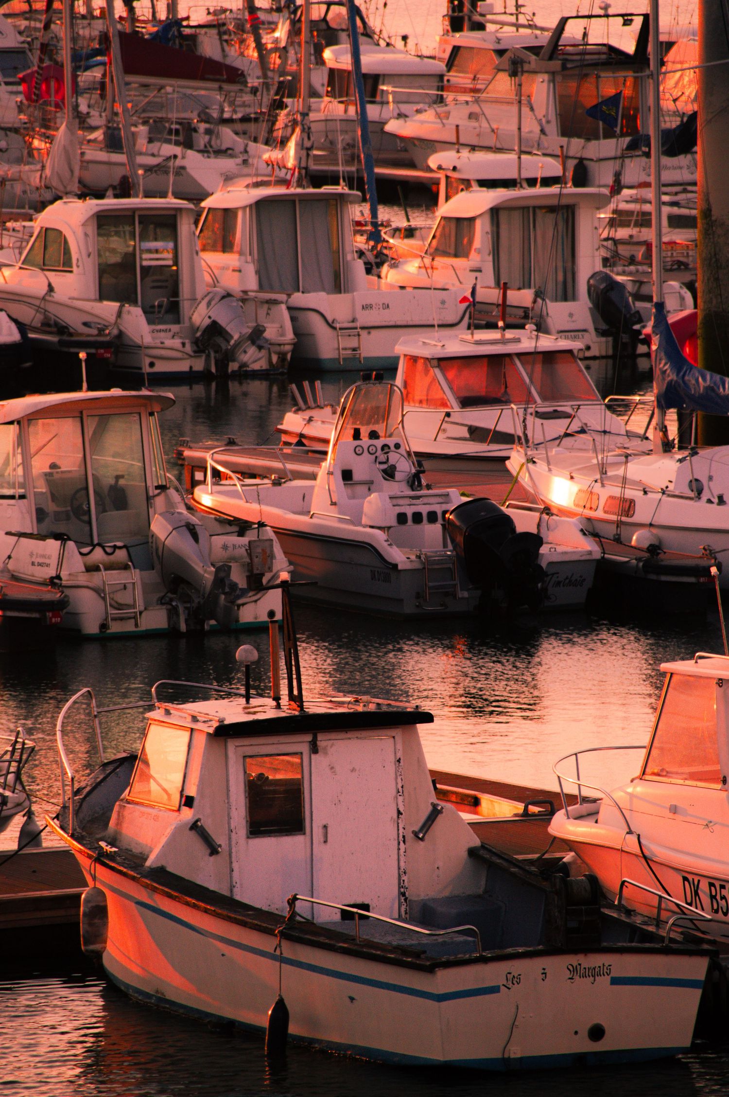 Boats docked in a marina at sunset with warm orange lighting reflecting off the water and vessels.