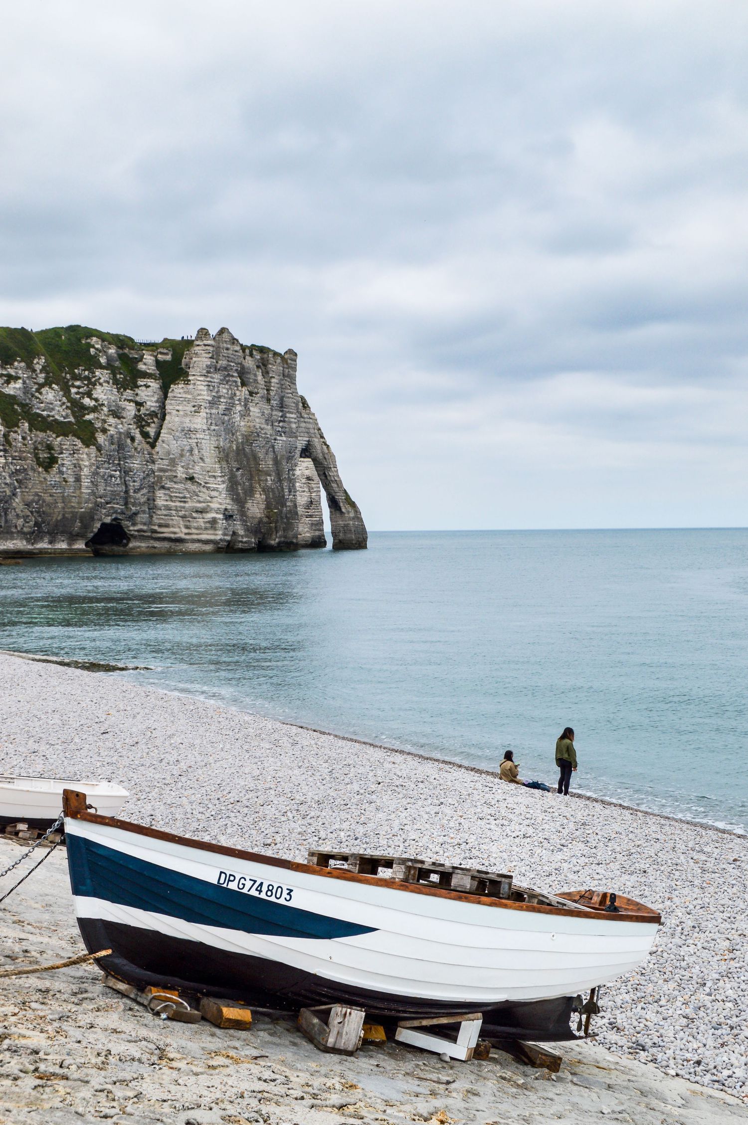 White boats resting on a pebble beach with dramatic chalk cliffs in the background.