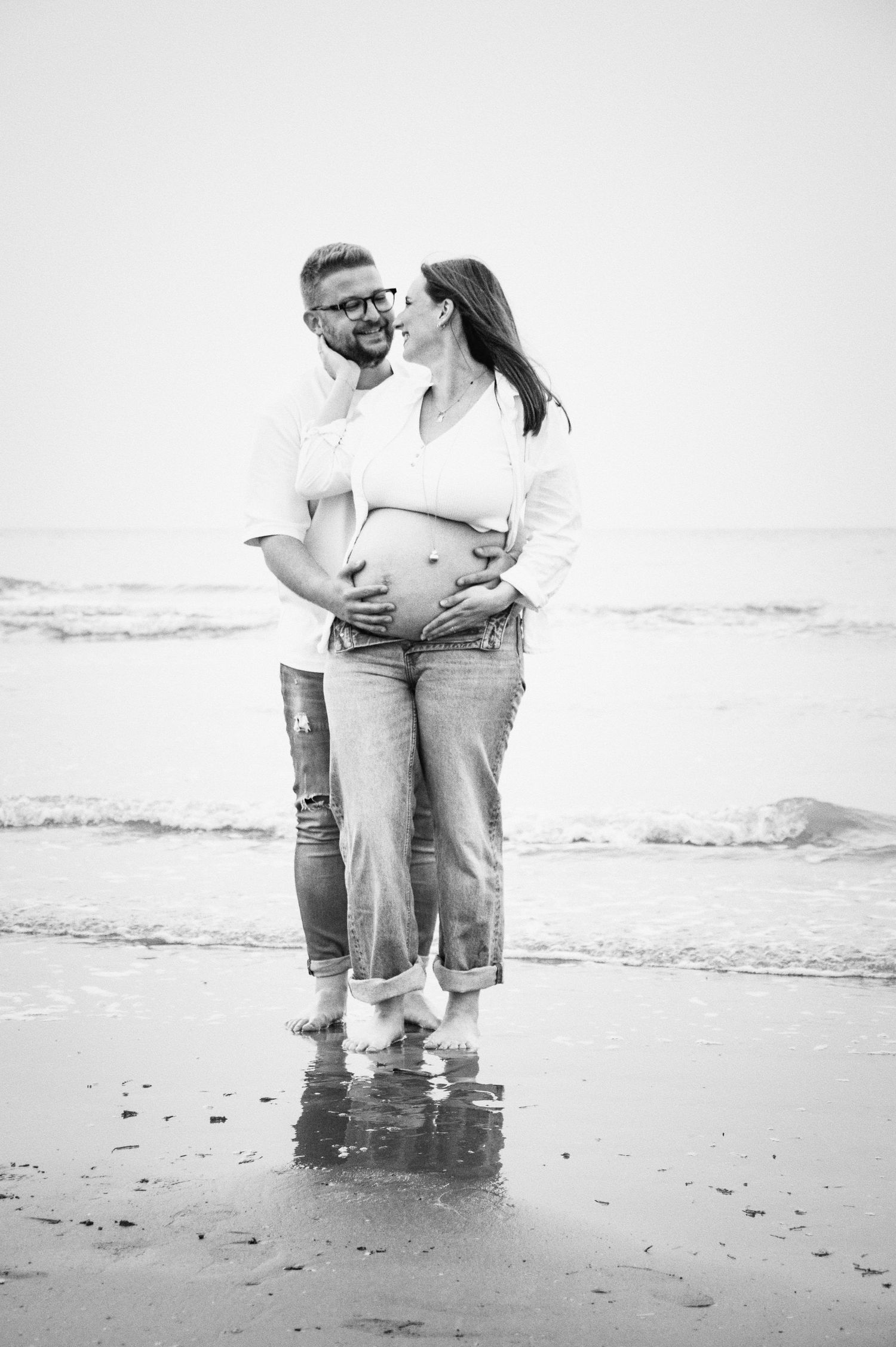 A black and white beach photo series captures tender moments between a couple by the ocean.