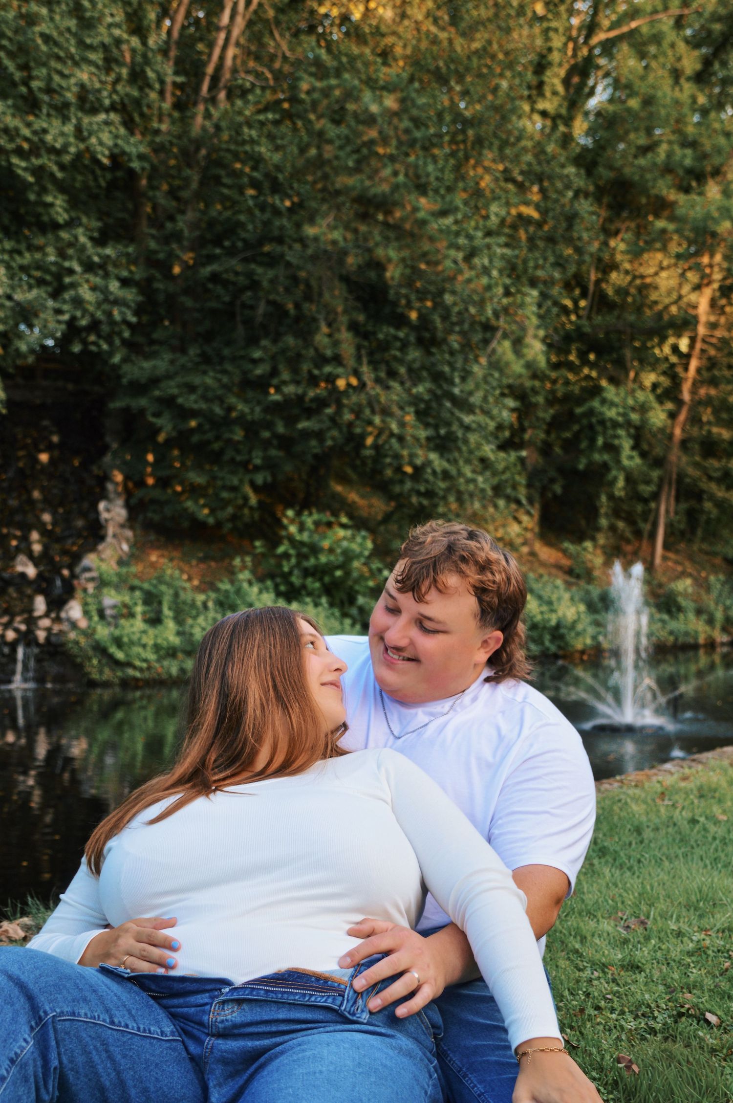 Couple lounging on grass near a fountain during outdoor photo session.