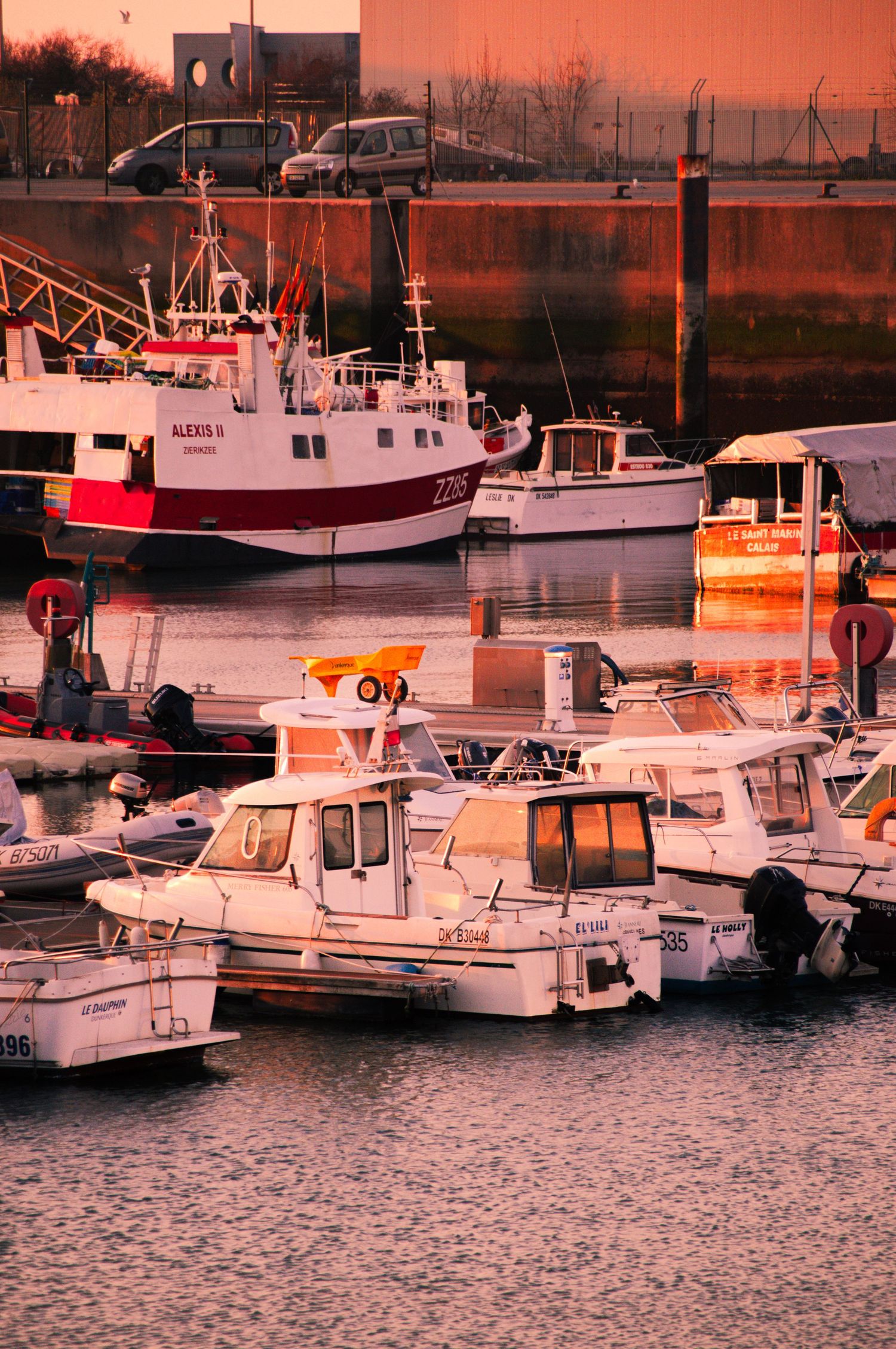 Multiple recreational boats and fishing vessels moored at a marina bathed in warm orange sunset light.