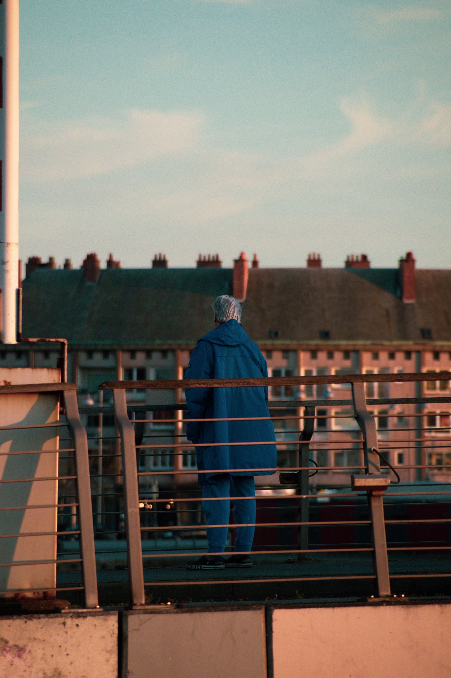 A person in blue sits on a bench overlooking rows of brick houses on a cloudy day.
