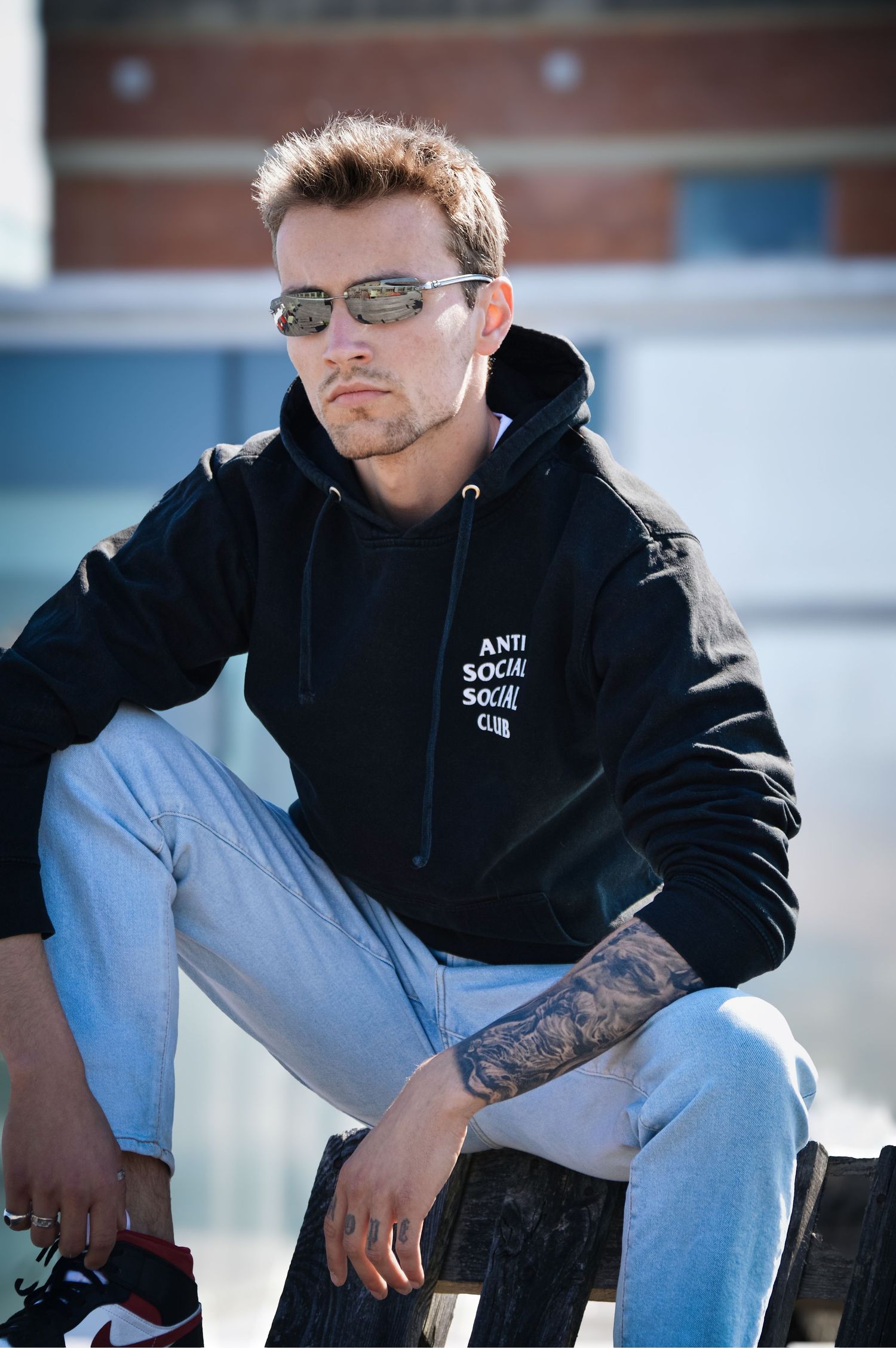 Person in black hoodie and jeans sitting casually outdoors.