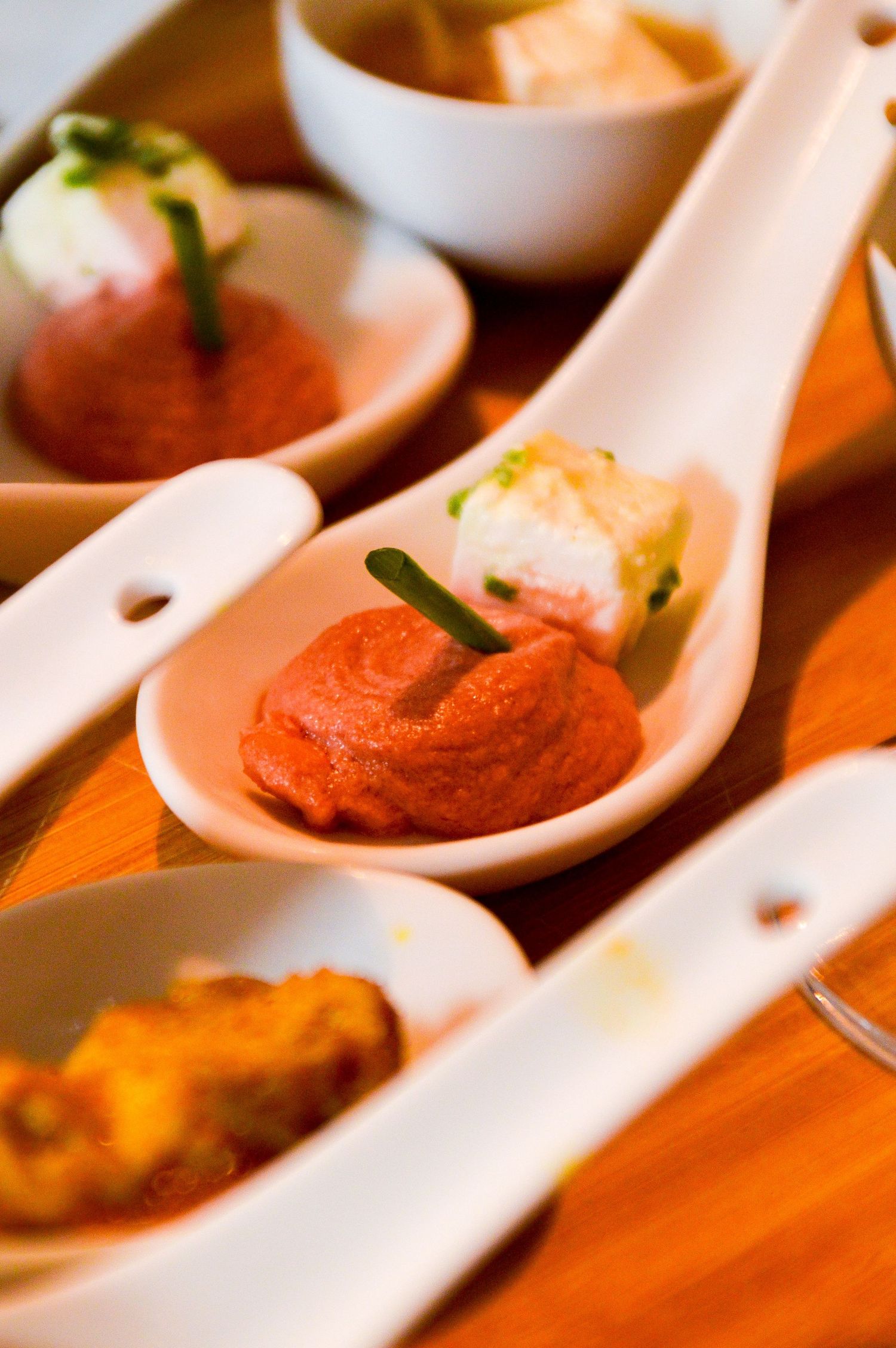 Elegant appetizers served on white ceramic spoons with colorful garnishes.