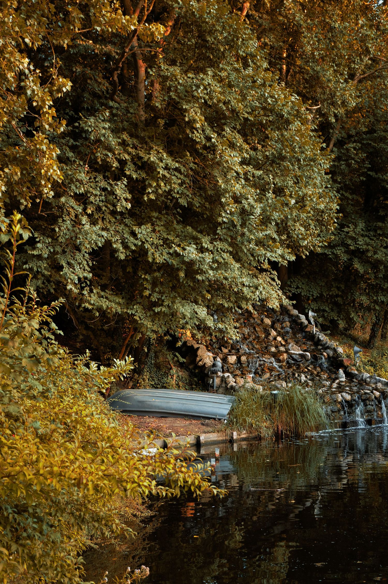 Small boat moored near autumn trees reflecting in calm lake waters during golden hour.