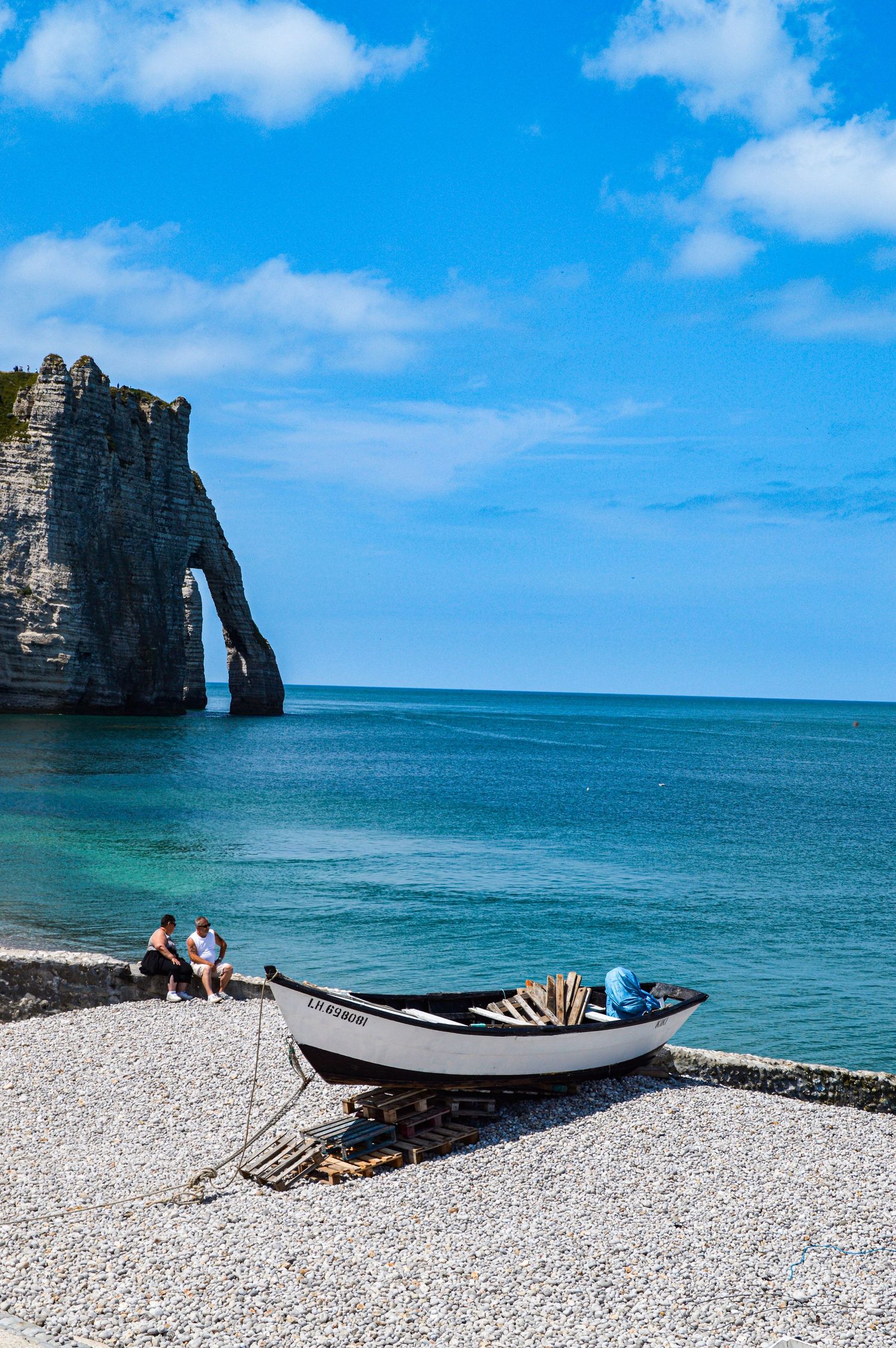 Coastal scene with boat on pebble beach near dramatic rocky cliffs and turquoise ocean.