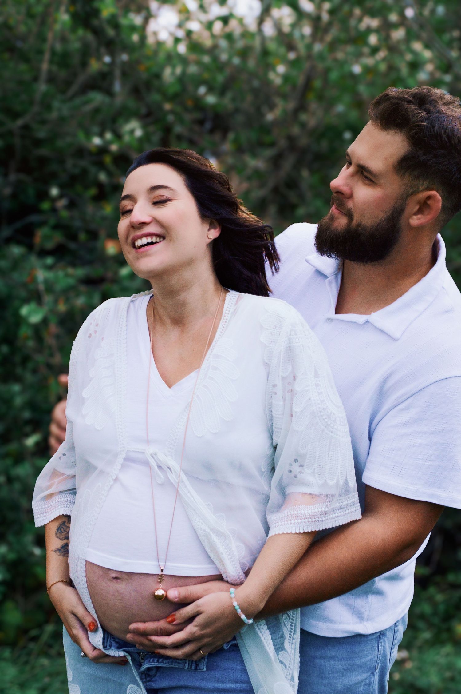 Candid maternity moments captured in white outfits against green foliage.