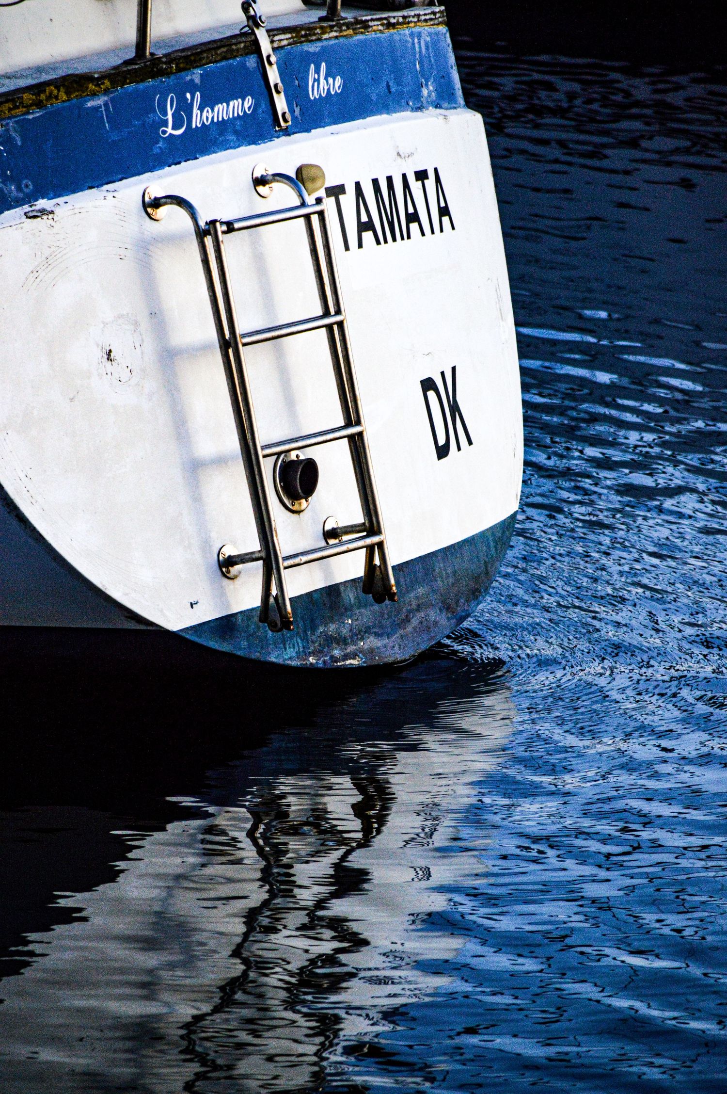 Close-up of boat hull with reflection in blue water showing partial name.