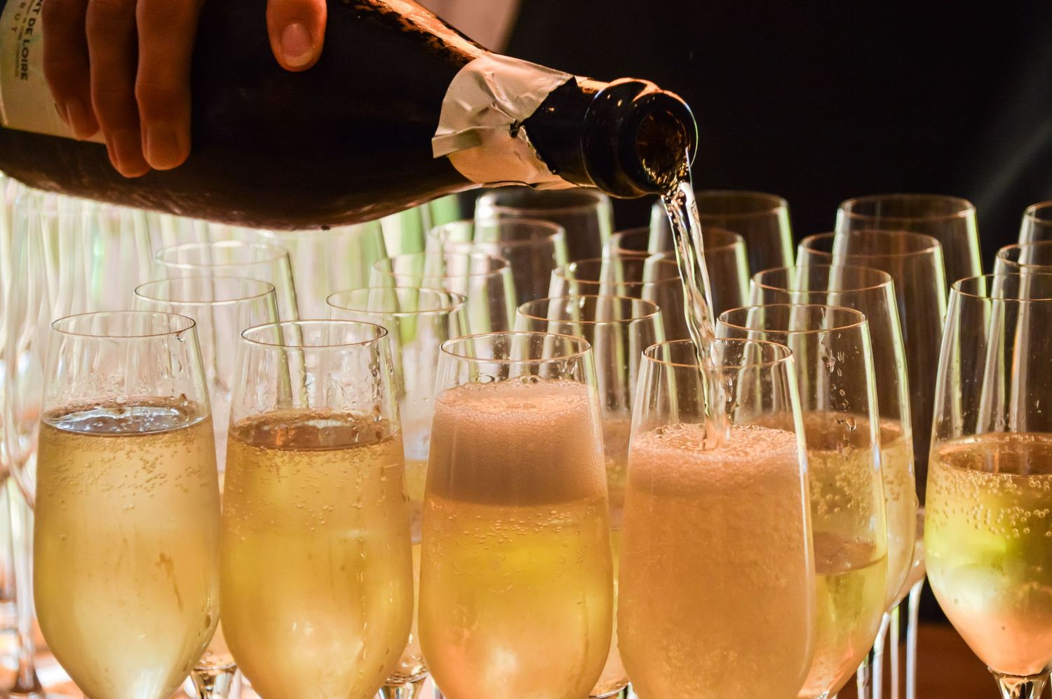 Champagne being poured into row of flutes creating golden bubbles.