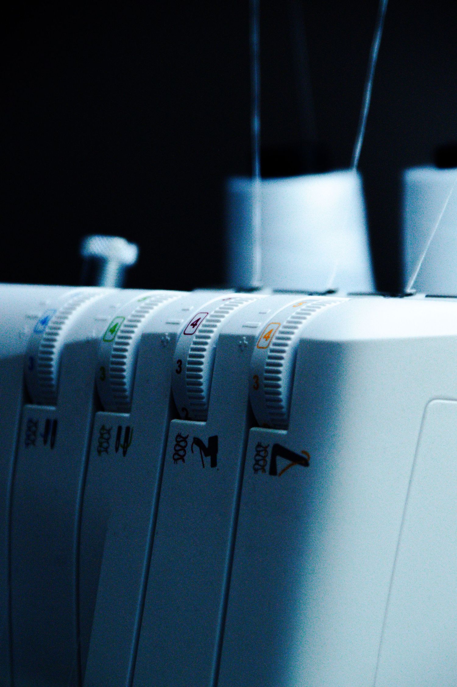 Close-up of a serger overlock sewing machine with tension dials and thread spools in blue tones.