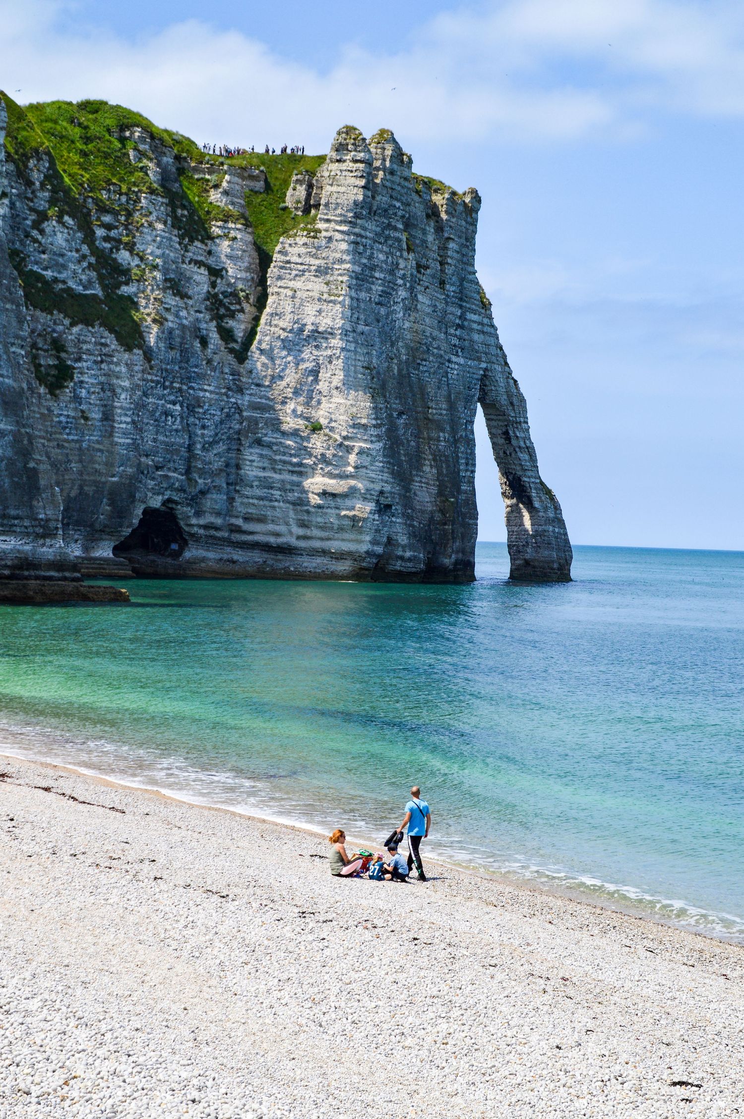 The iconic Etretat arch and limestone cliffs frame visitors enjoying the pebbly beach below.