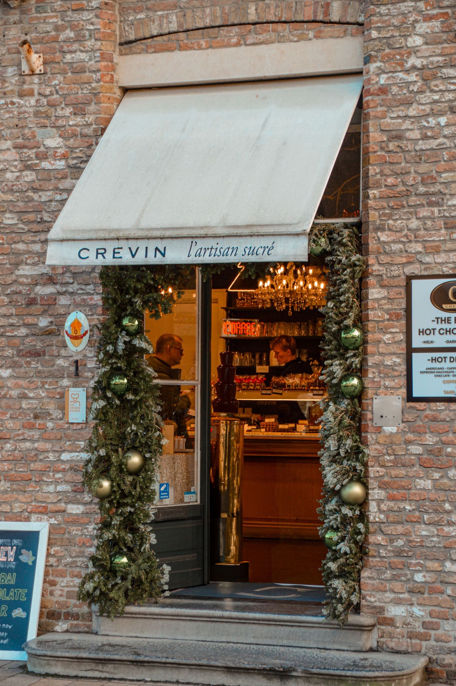 Brick storefront of Crevin shop with elegant holiday greenery decorations and warm lighting.