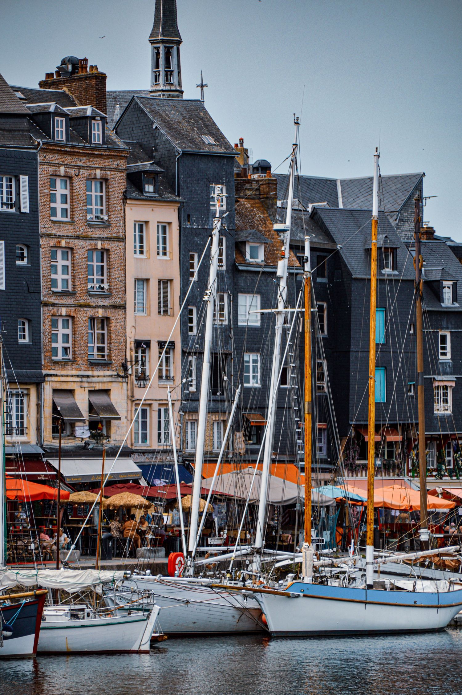 Historic waterfront buildings and moored sailboats in a French harbor town.