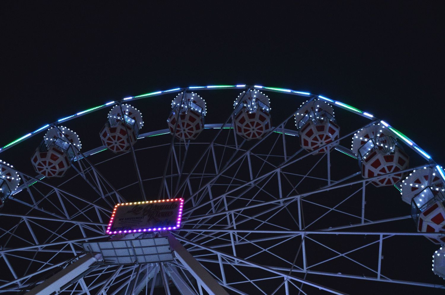 Illuminated Ferris wheel against dark night sky with neon lights.