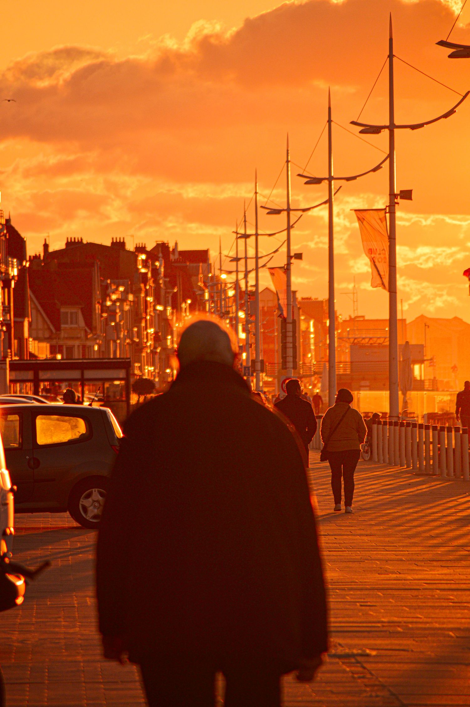 Silhouettes of people walking on a boardwalk during a vibrant orange sunset.