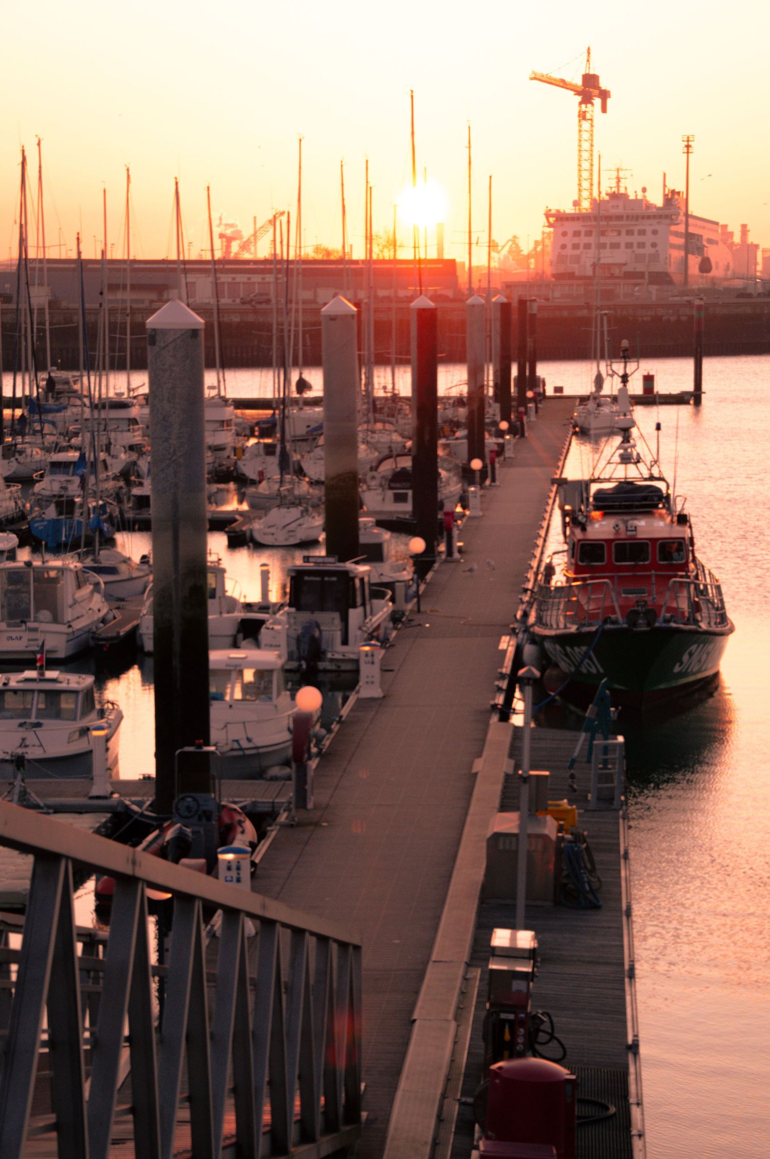 Boats docked at a marina during golden sunset with silhouetted masts and wooden piers stretching into calm waters.
