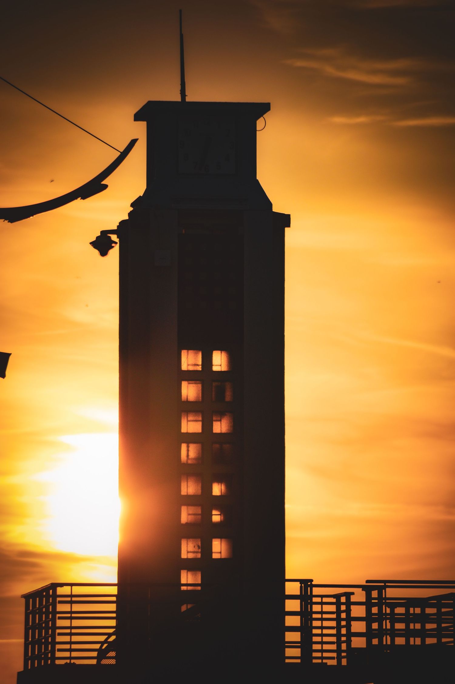 A silhouetted tower stands against a vibrant orange sunset sky.