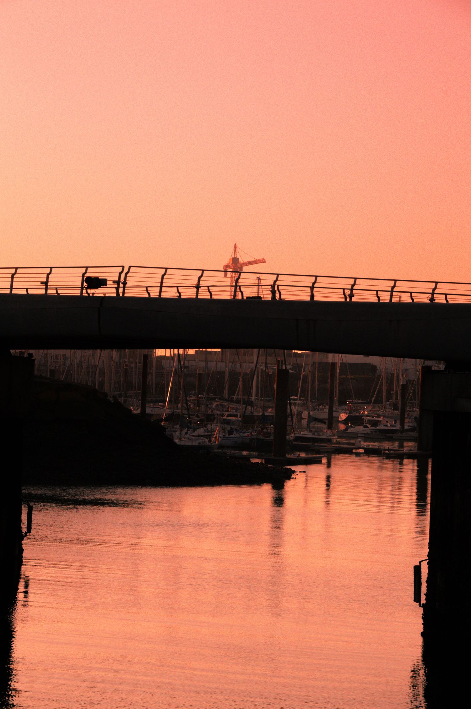 Silhouette of a marina dock with boats at sunset creating a peaceful orange and pink reflection on calm waters.