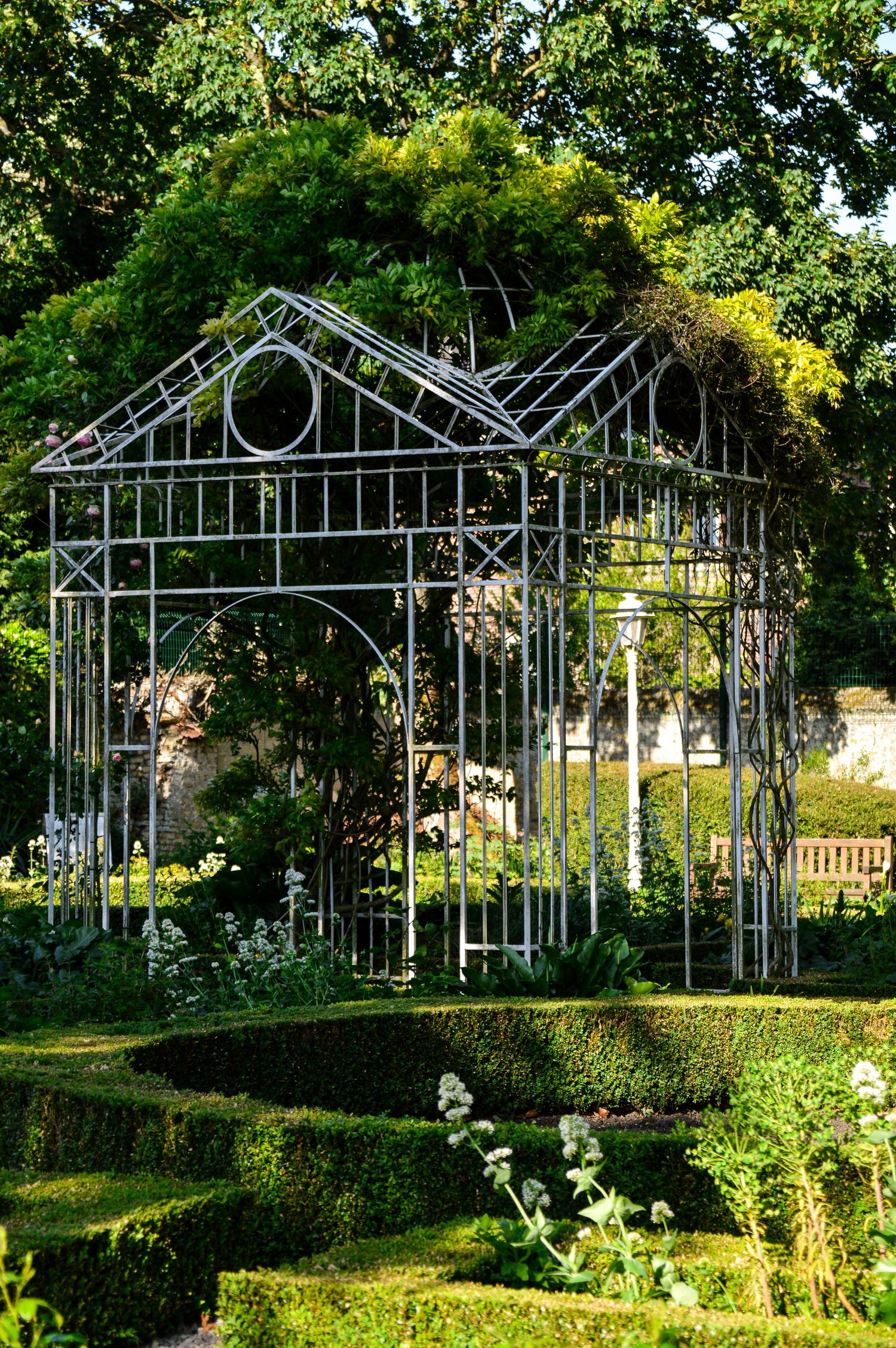Series of ornate metal gazebos arranged in a garden setting with green foliage.
