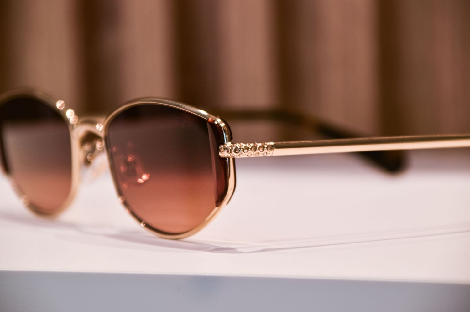 Detailed view of gold-framed sunglasses with rose gradient lenses showing decorative temple design.