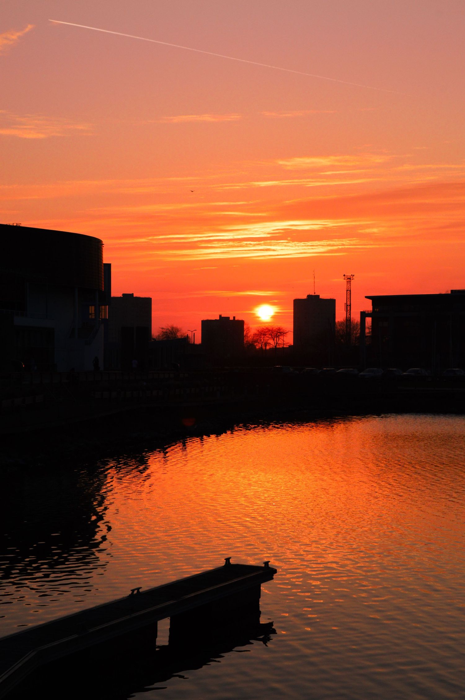 Front de mer urbain avec un quai en silhouette sur un ciel spectaculaire de coucher de soleil orange et rouge.