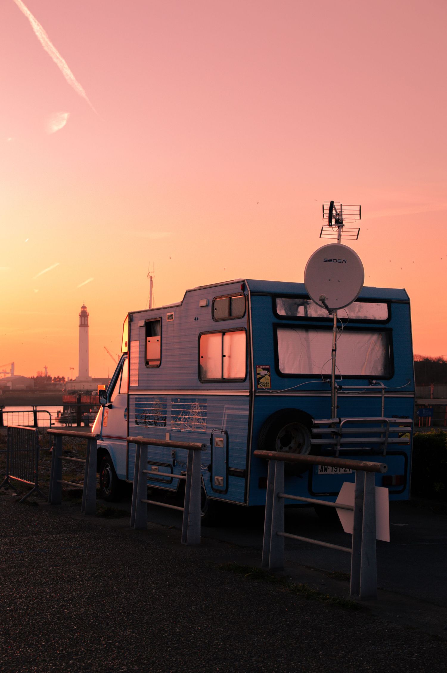 A row of RVs and campers parked at a campground silhouetted against a pink and orange sunset sky.