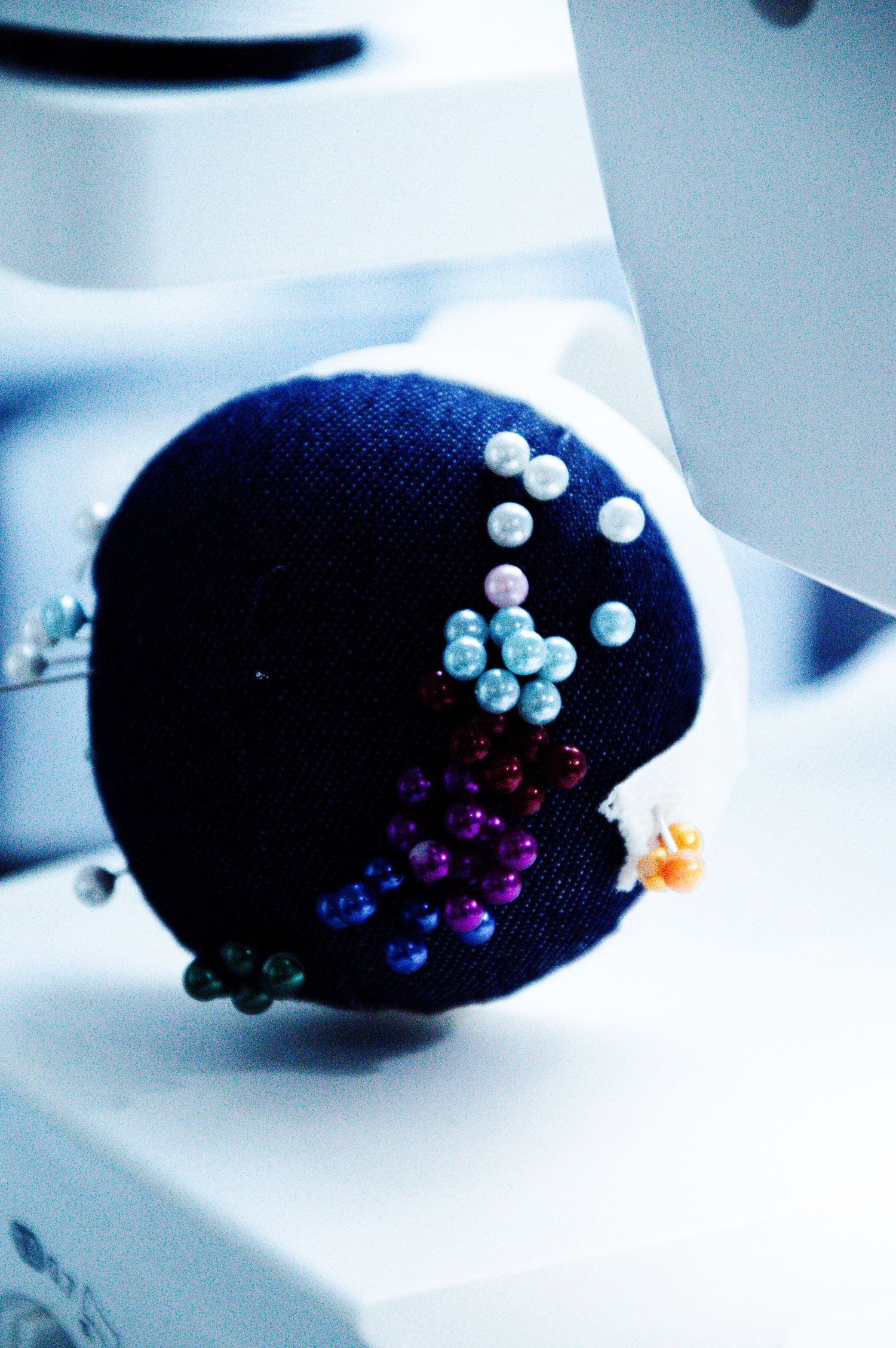 A dark blue fabric pincushion adorned with colorful beaded pins near a sewing machine.