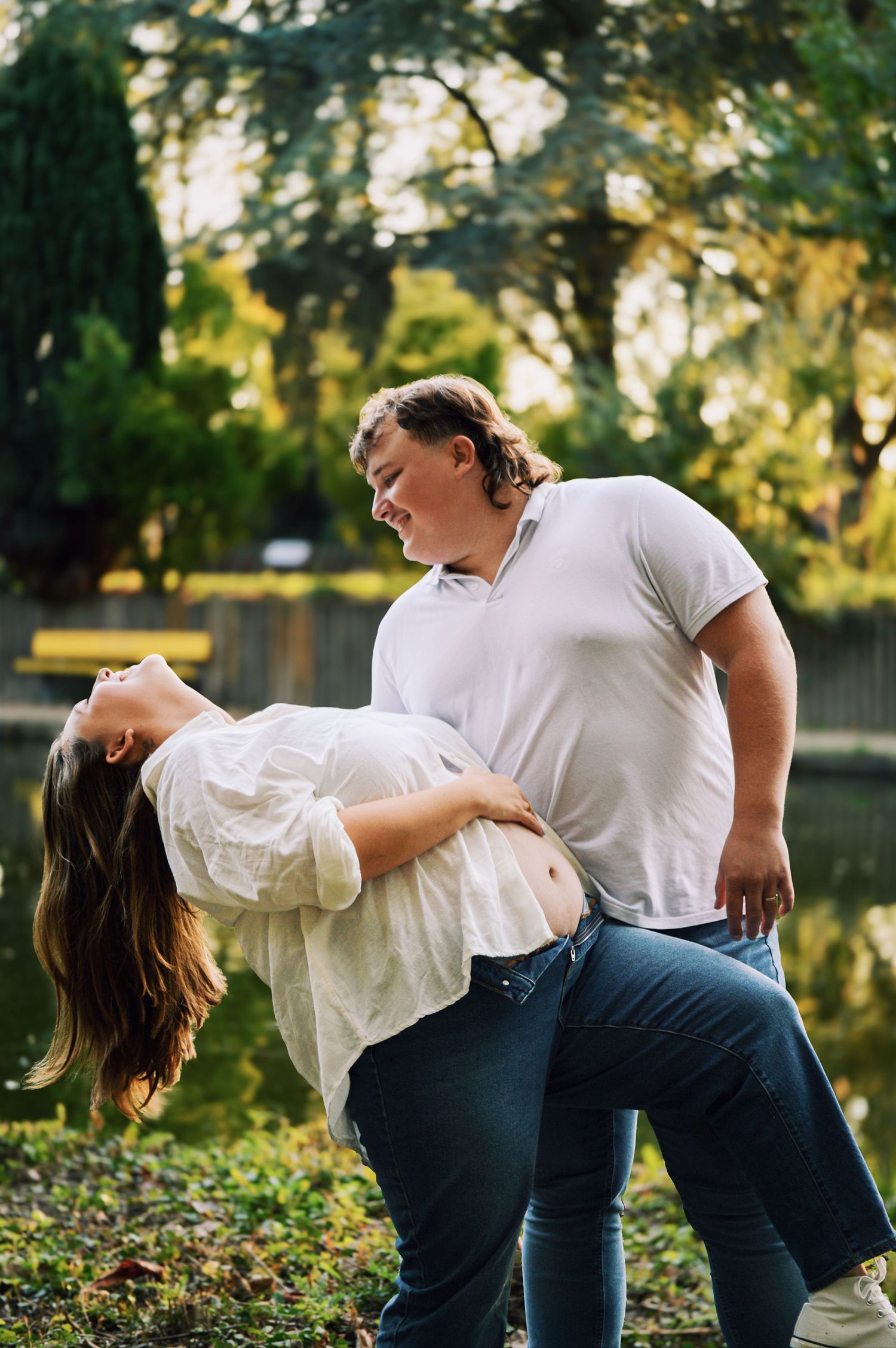 A couple performs romantic dance dips in a sunlit garden setting wearing casual attire.