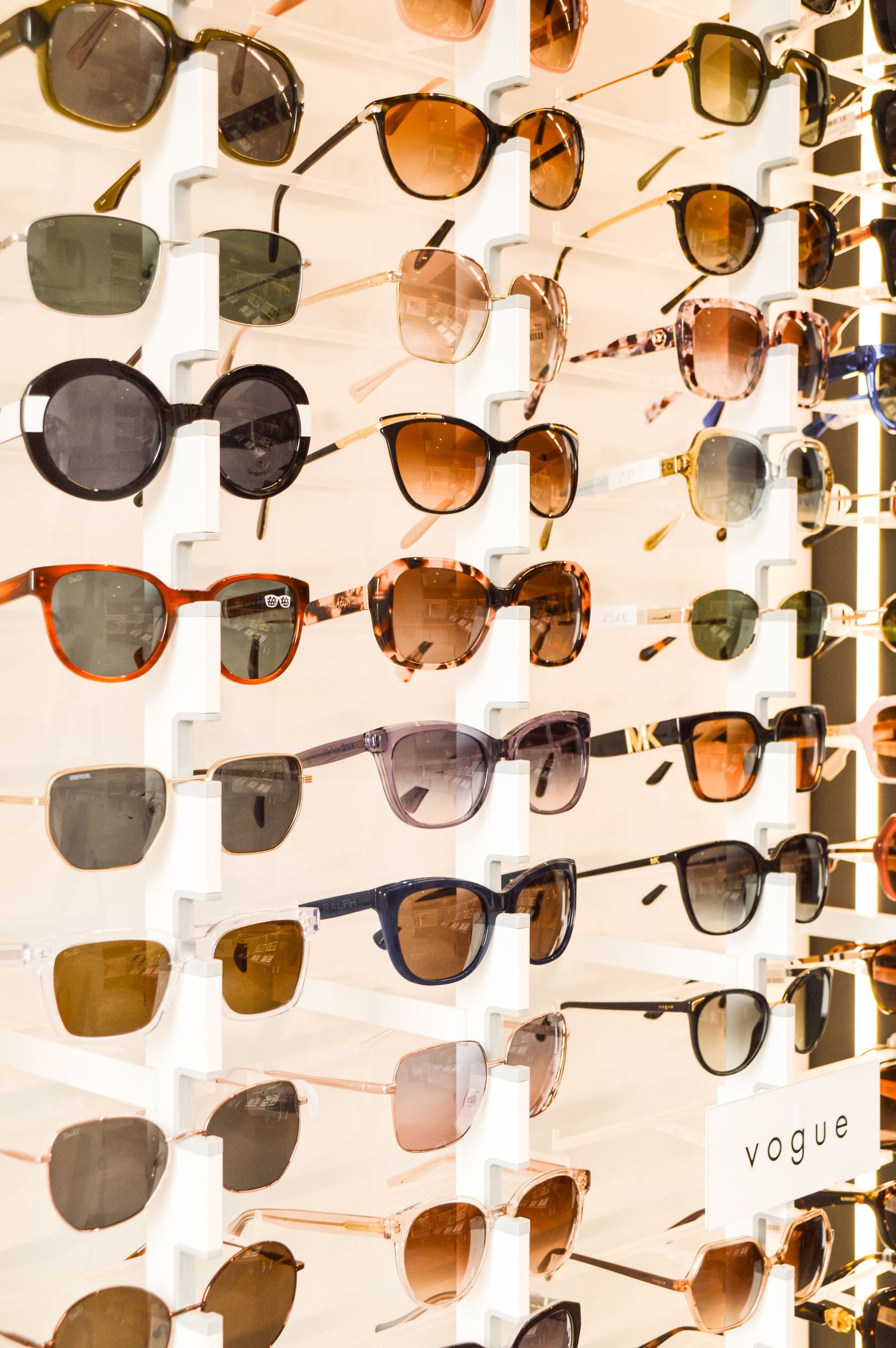 Rows of designer sunglasses displayed on white retail wall mount with various styles and tints.