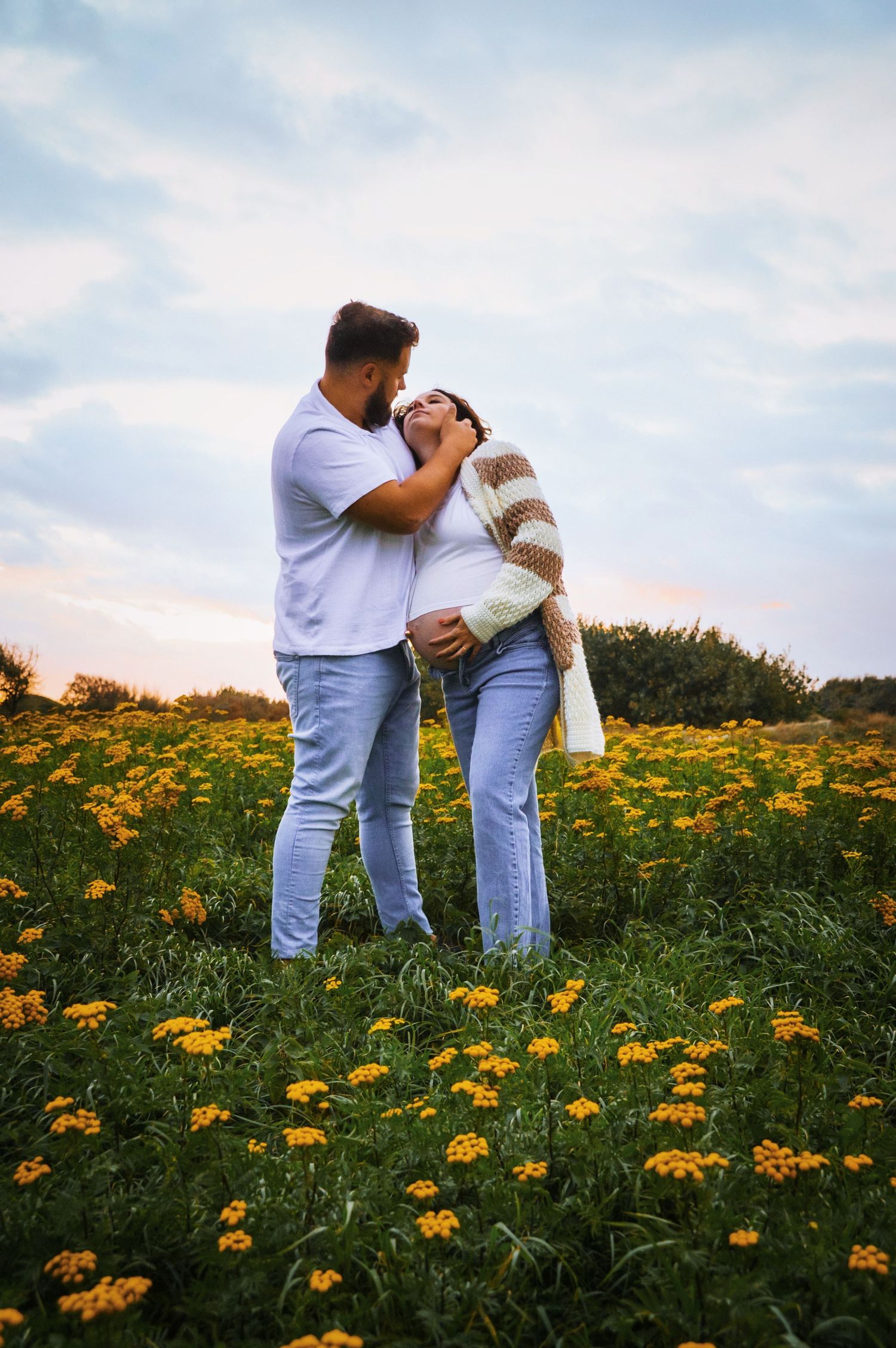 Romantic couple poses in meadow filled with bright yellow flowers.