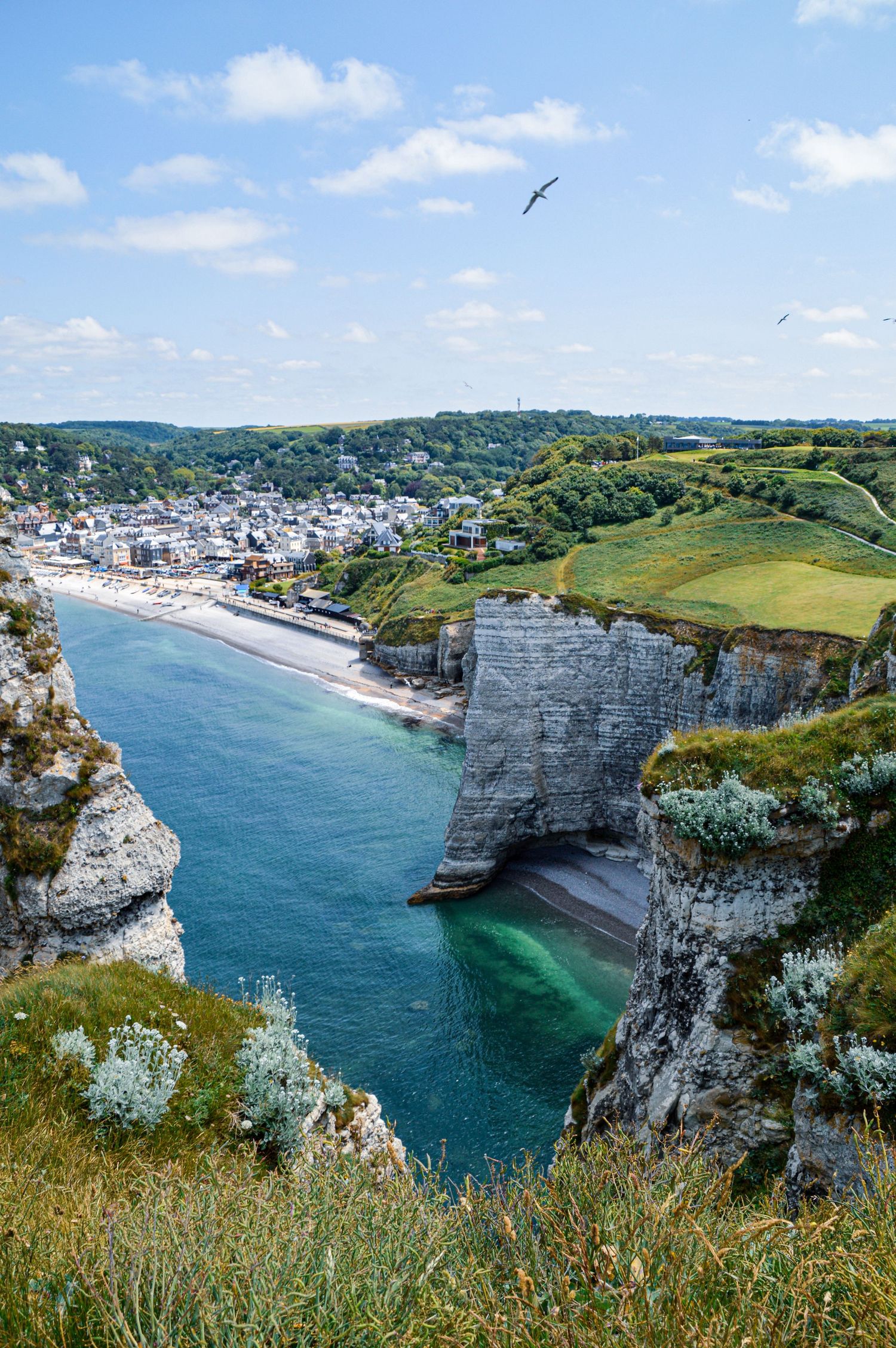 Dramatic white chalk cliffs and coastline overlooking turquoise waters and a seaside town in Normandy, France.