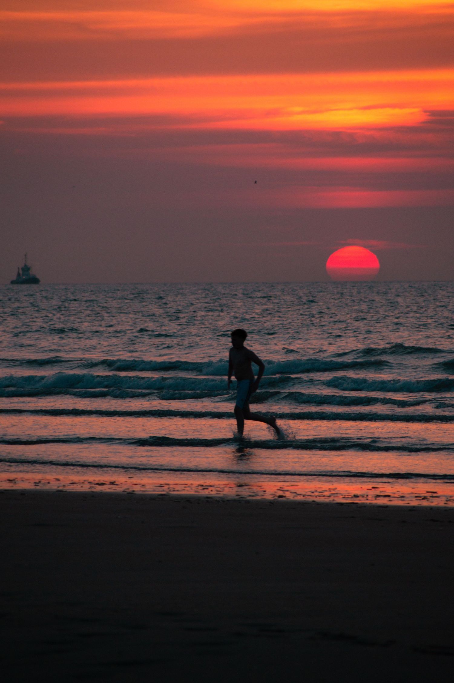 Silhouette of a person running on a beach at sunset with a vivid red and orange sky and sun setting over the ocean.