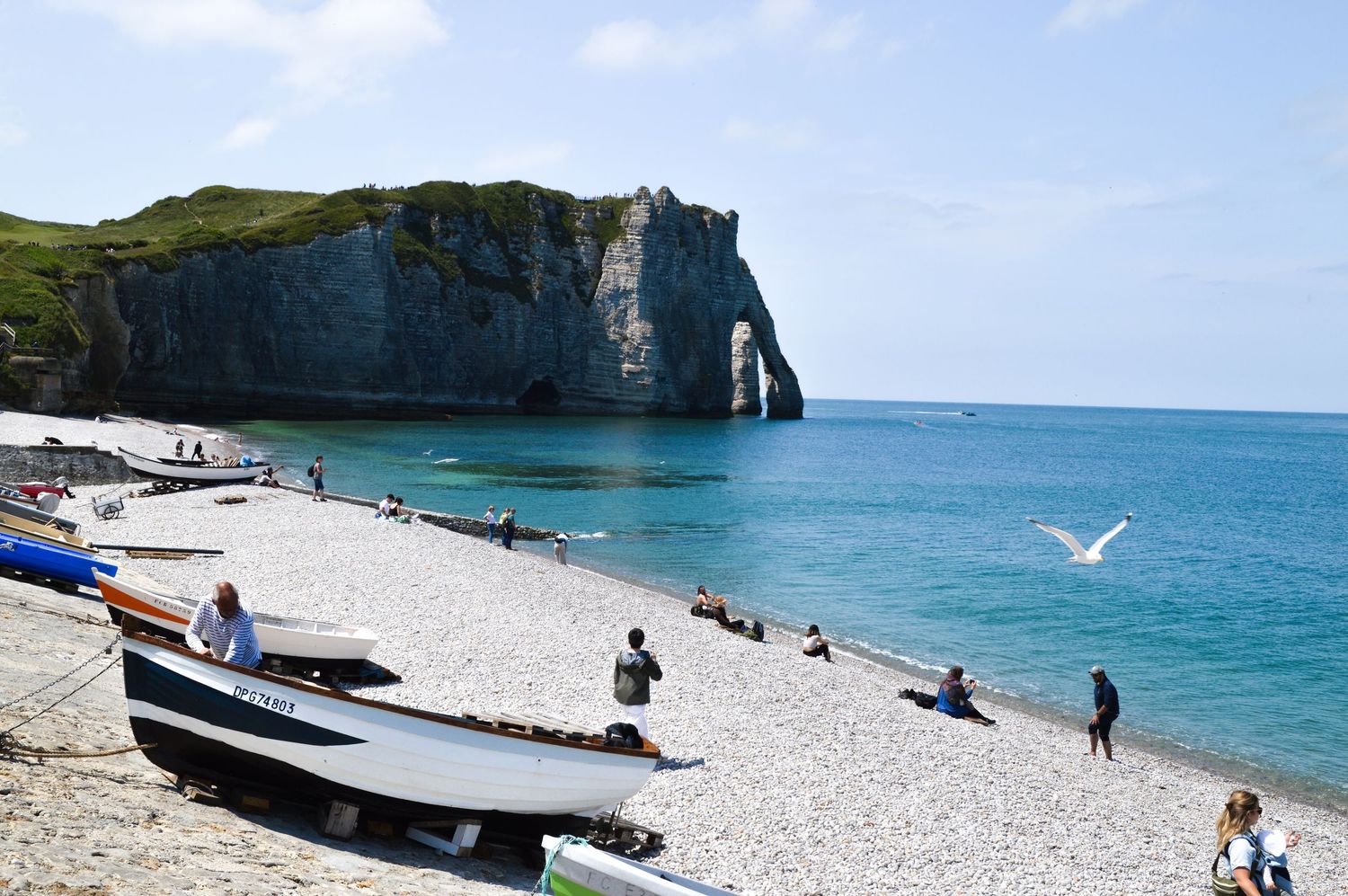Boats line the pebble beach as visitors enjoy views of the dramatic Etretat cliff arch.