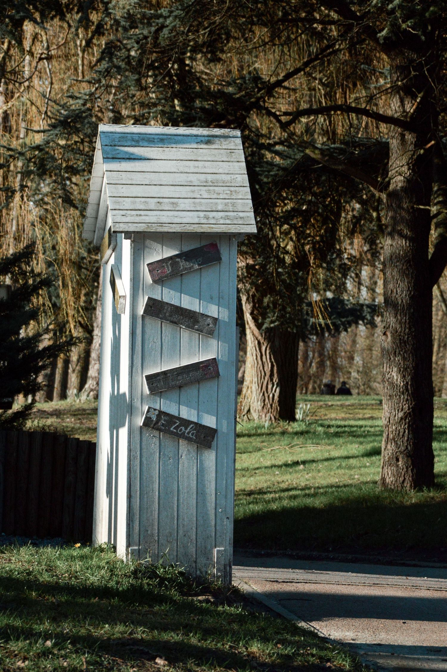 Small white wooden outhouse structure nestled among trees in a park setting.