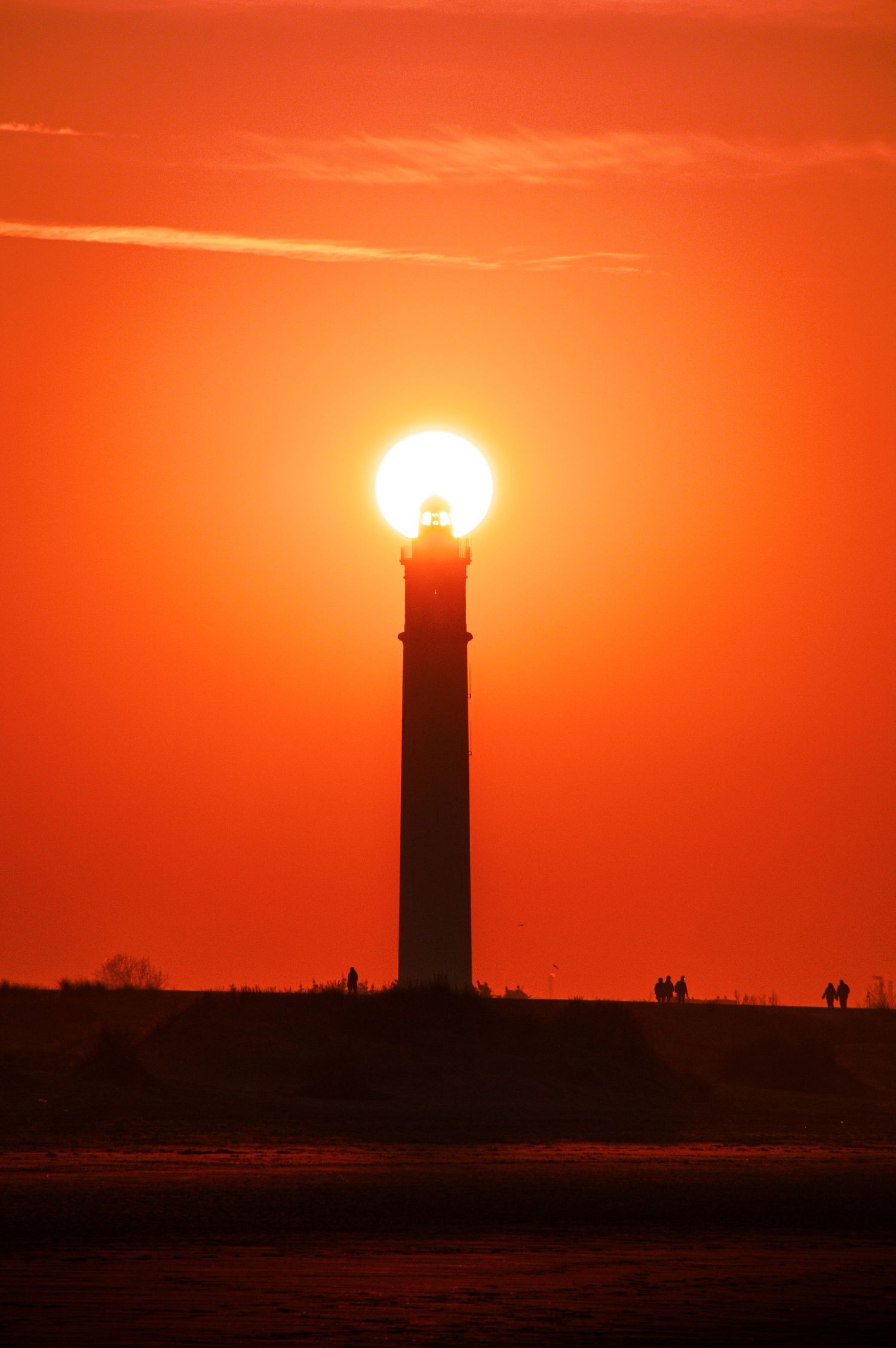Phare en silhouette sur un coucher de soleil orange parfait, avec le soleil semblant reposer au sommet de la tour.